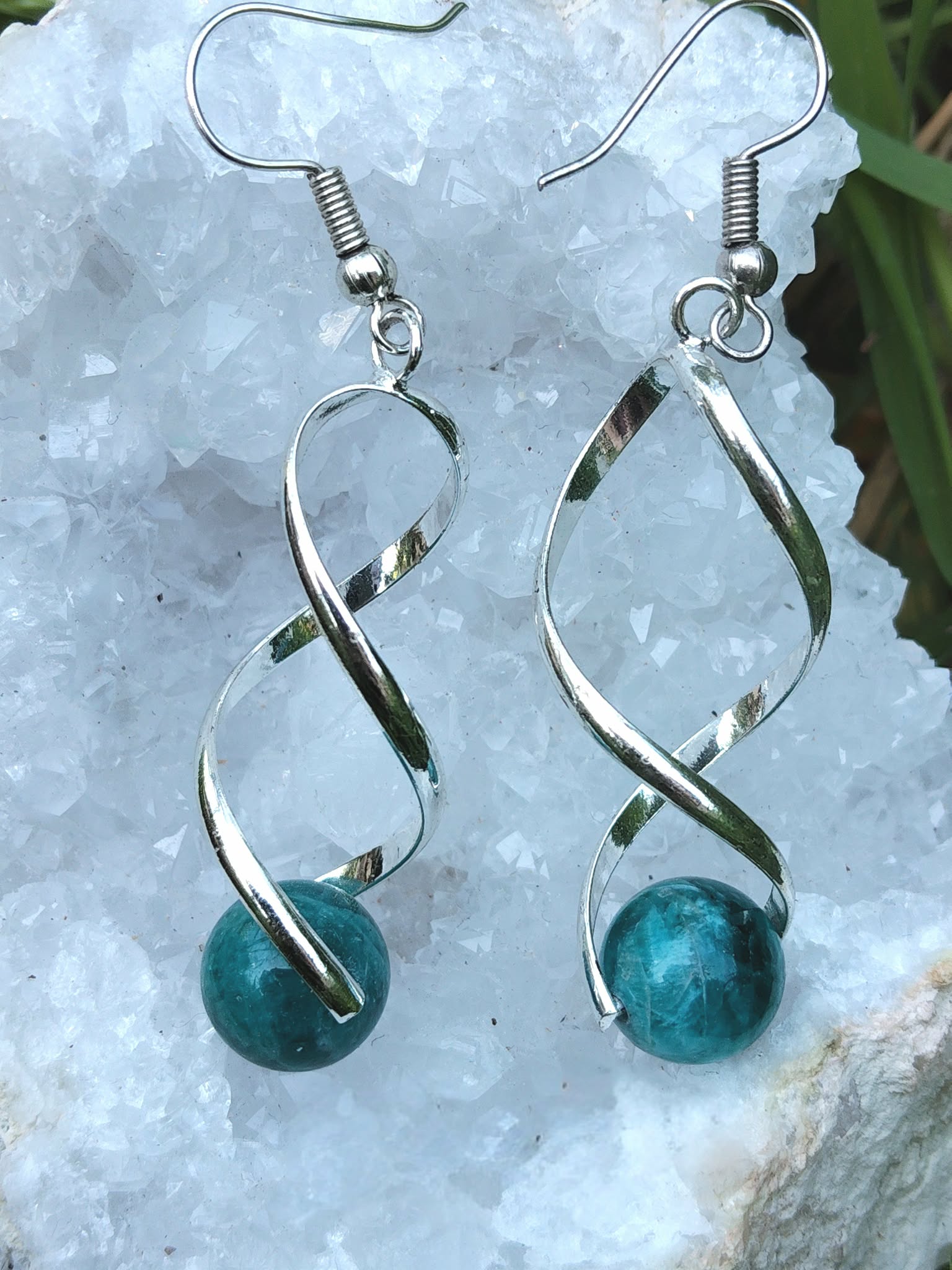 Boucles d’oreilles spirales argentées avec perles d’apatite bleue posées sur géode, clarté, motivation, communication.