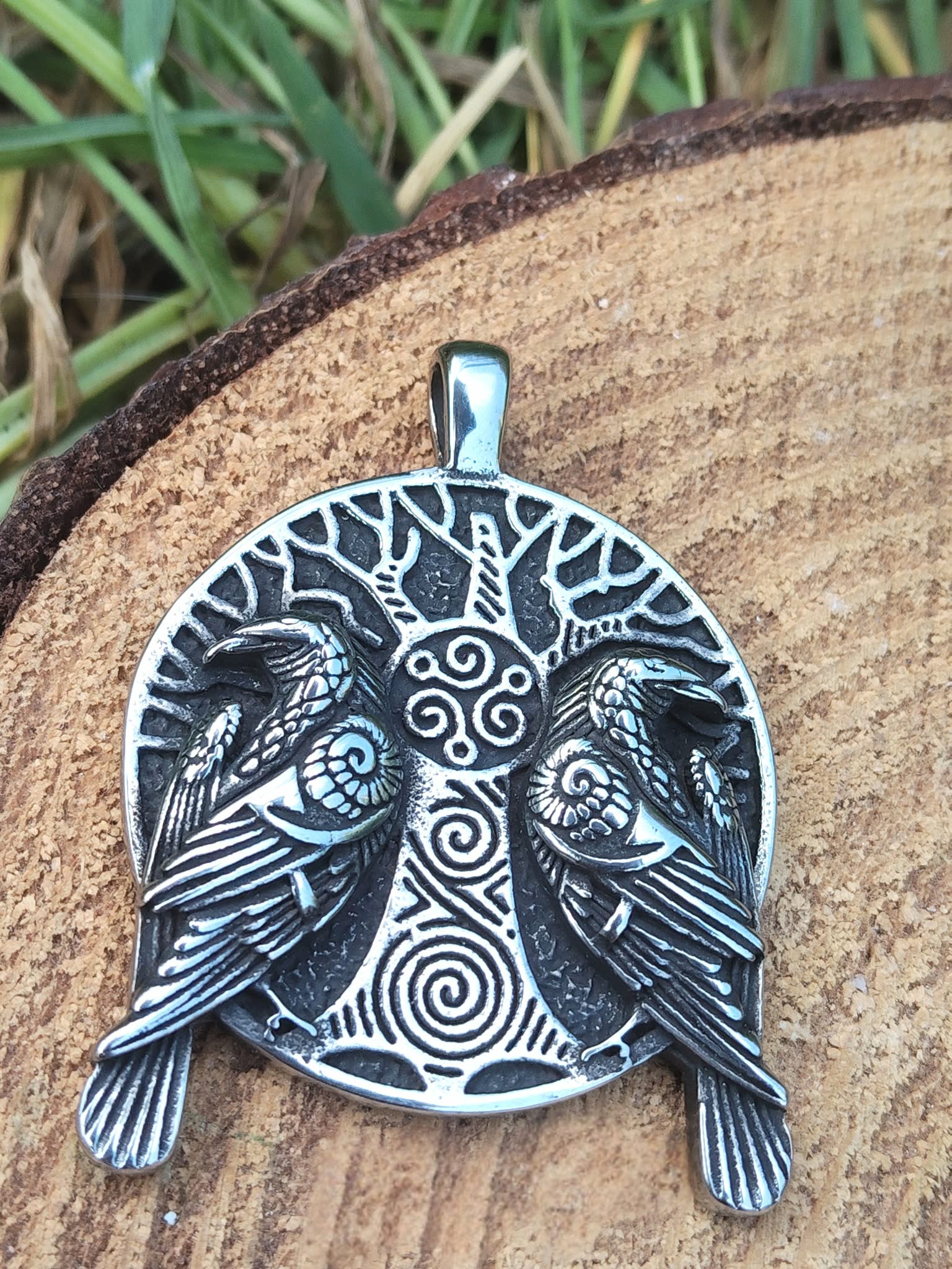Pendentif viking verso argenté noirci avec gravure arbre sacré et spirales, posé devant mousse, feuillage vert et pierre blanche