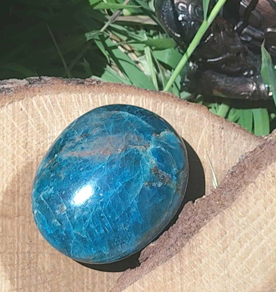 Galet d’apatite bleue polie ovale présenté dans un pochon beige avec feuillage en arrière-plan, pierre naturelle évoquant la douceur émotionnelle, la concentration et l’inspiration.