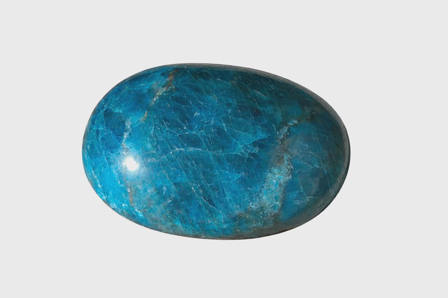Galet poli ovale en apatite bleue sur fond blanc, surface brillante aux marbrures naturelles, pierre fine reliée à la lucidité, à la parole fluide et à la confiance tranquille.