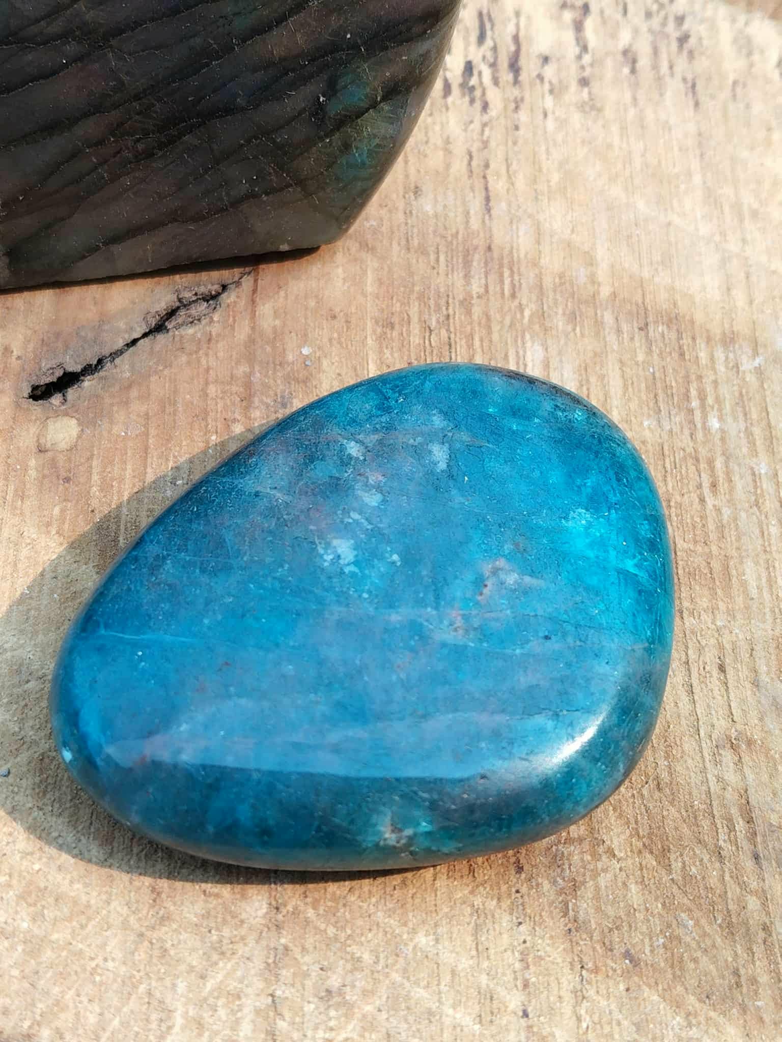 Galet d’apatite bleue poli sur support en bois avec plume noire, pierre naturelle associée à la lucidité, à l’expression posée et à l’équilibre intérieur.