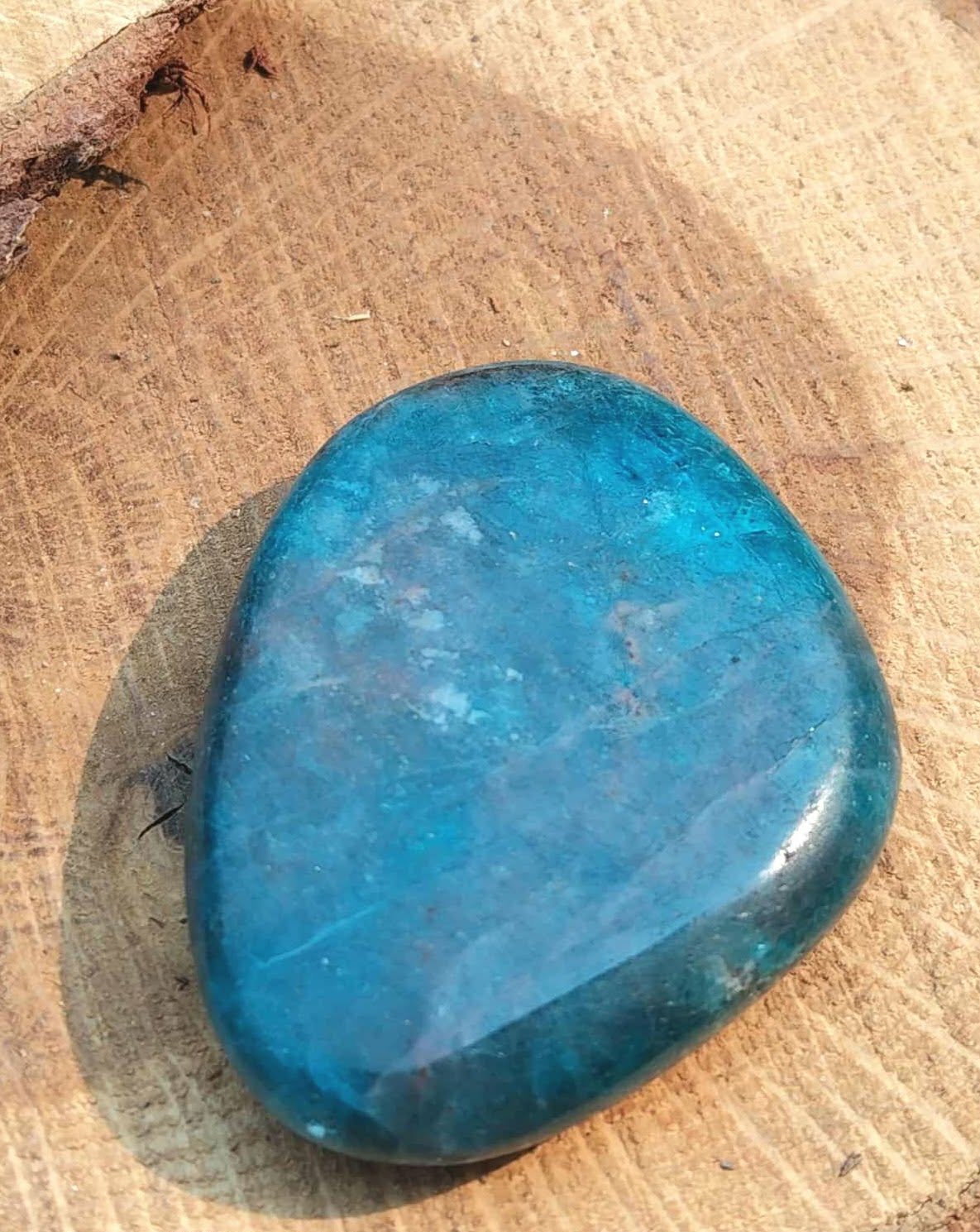 Galet d’apatite bleue poli posé sur support en bois clair, pierre naturelle reliée à la présence à soi, à la clarté d’esprit et au dynamisme doux.
