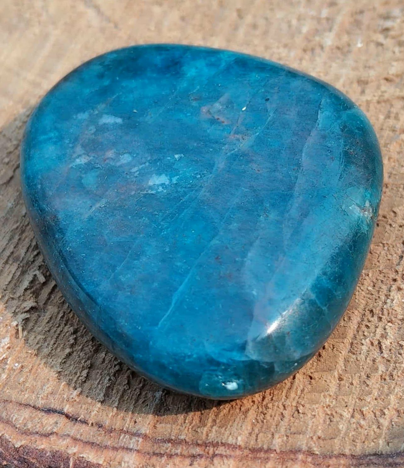 Galet d’apatite bleue polie bleu profond posé sur support naturel texturé, pierre naturelle associée à la profondeur intérieure, à l’aisance d’expression et au calme du mental.