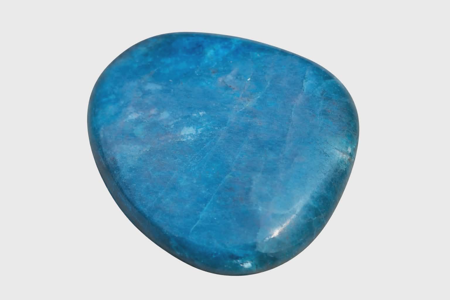 Galet d’apatite bleue poli sur fond blanc, pierre naturelle reliée à la sérénité, à la parole fluide et à la confiance tranquille.