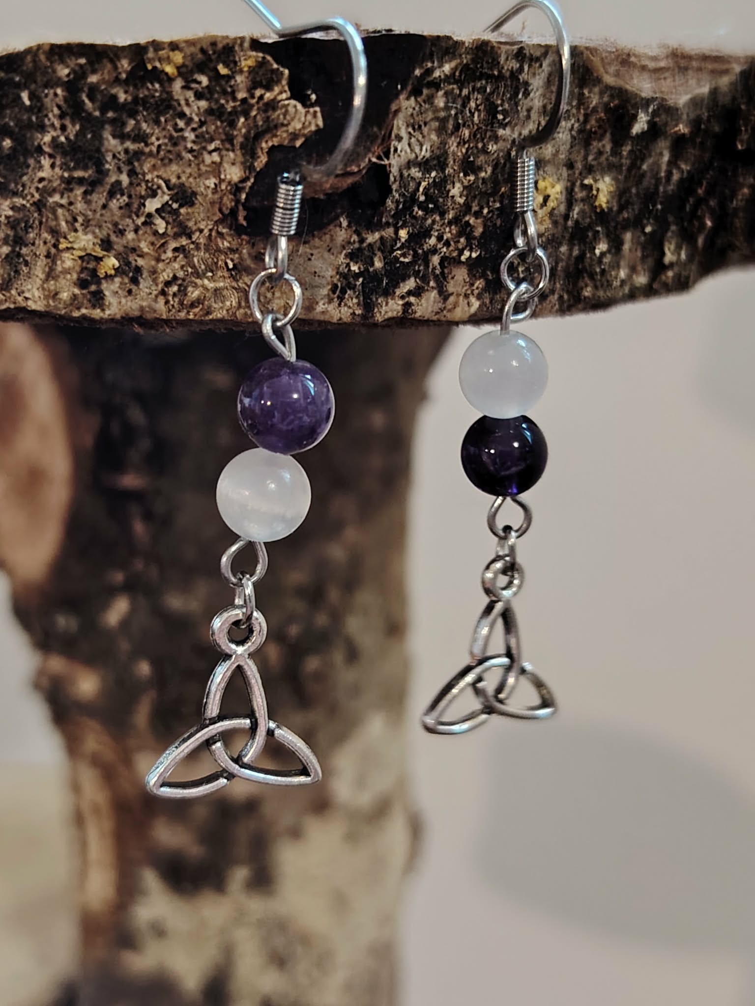 Création Magic Gaïa – boucles d’oreilles pendantes triquetra argenté, perles d’améthyste et de sélénite, suspendues sur support naturel – apporte apaisement, clarté, intuition.