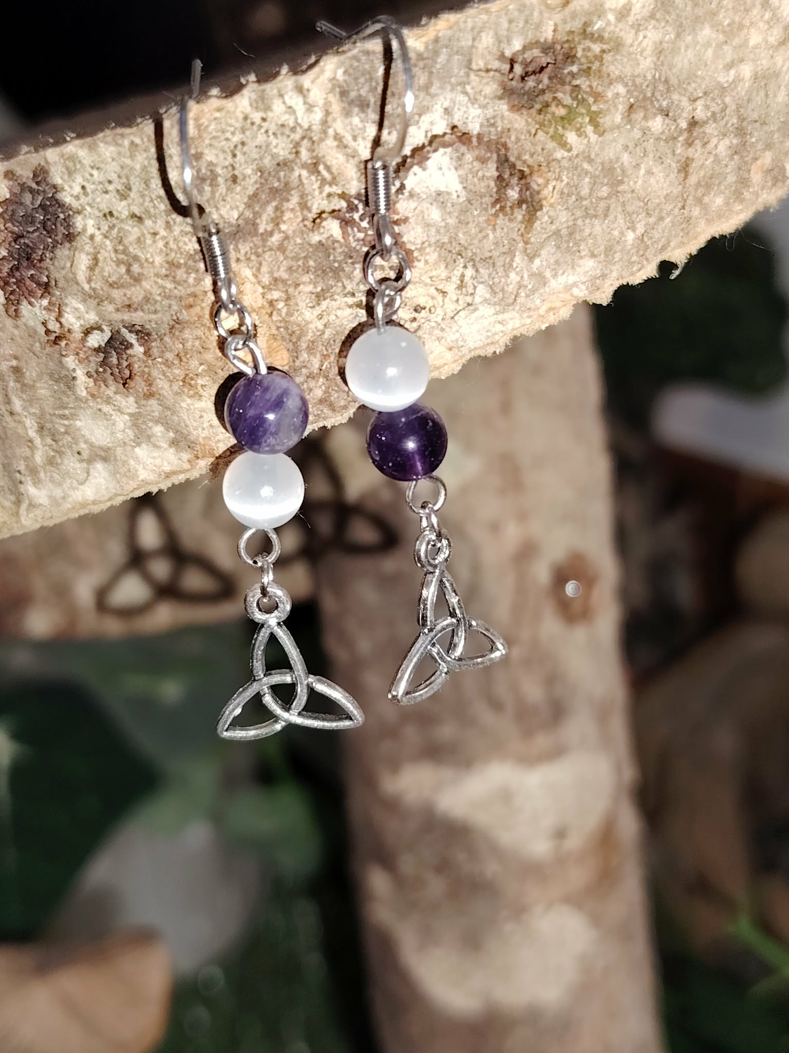 Création Magic Gaïa – boucles d’oreilles pendantes triquetra argenté, perles sélénite améthyste, suspendues sur support minéral – apporte apaisement, clarté mentale, intuition.