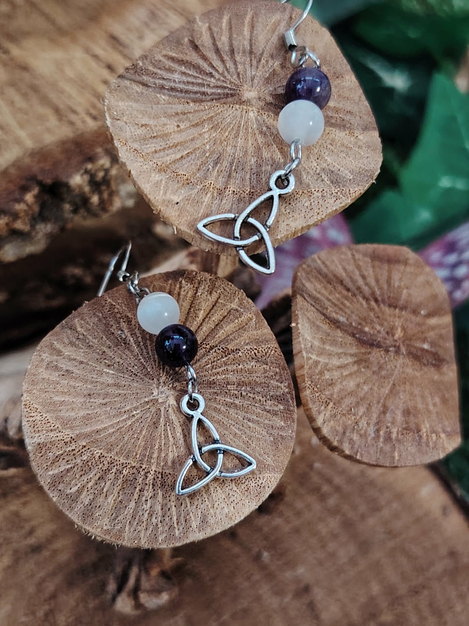 Boucles d’oreilles triquetra argenté avec perles d’améthyste et de sélénite, mises en scène sur champignon de bois en décor – Création Magic Gaïa – apporte apaisement, clarté, intuition.