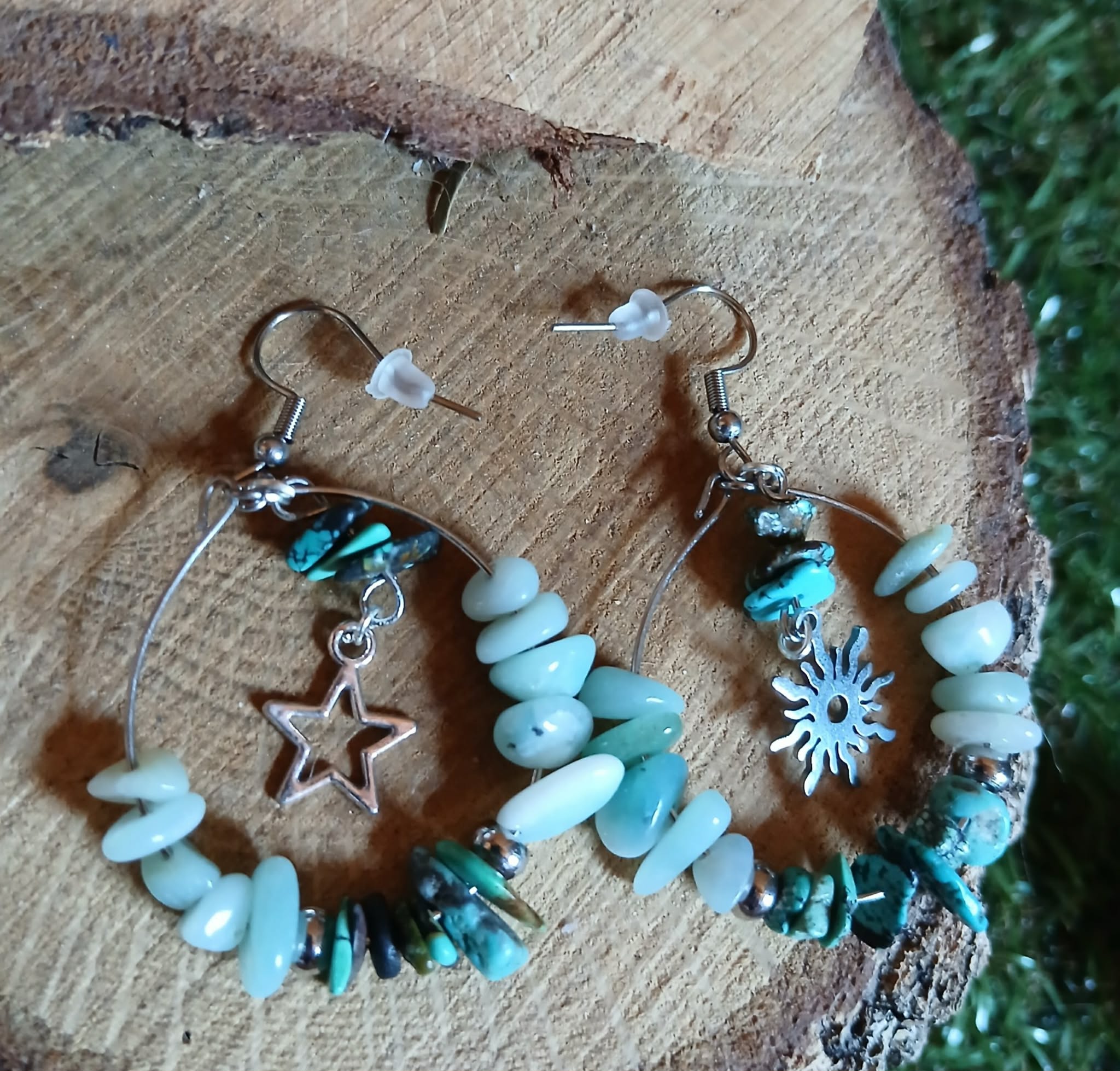 Boucles d’oreilles Ombre &amp; Lumière création Magic Gaïa, anneaux argentés avec amazonite et éclats de turquoise, charms étoile et soleil, photo sur rondin de bois avec feuillage.