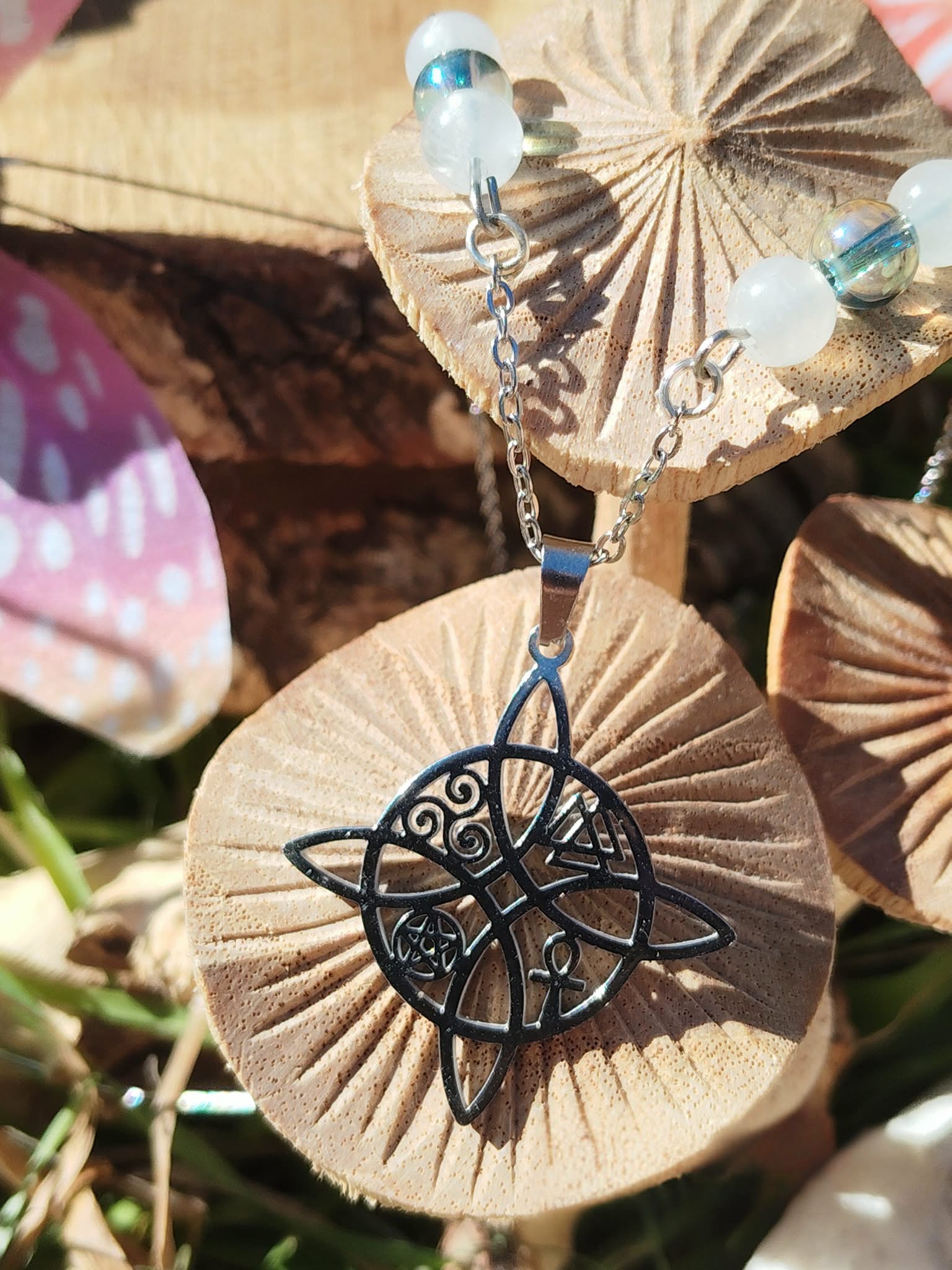 Collier nœud de sorcière avec péristérite et Aqua Aura sur décor nature avec champignons, clarté mentale et recentrage serein