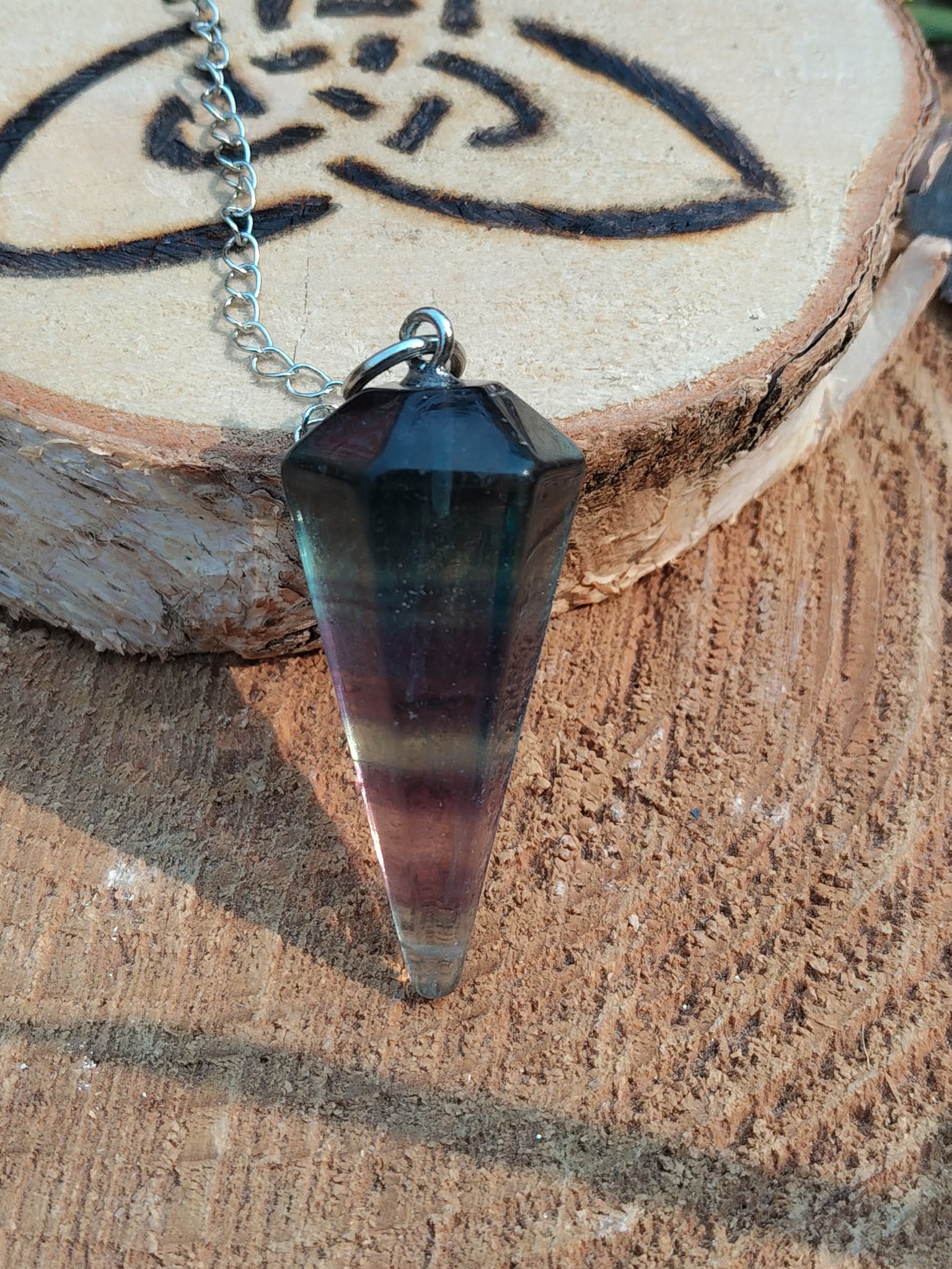 Pendule en fluorite facettée sur chaîne argentée, posé sur tranche de bois gravée, ambiance apaisante, aide à la clarté et à la concentration.