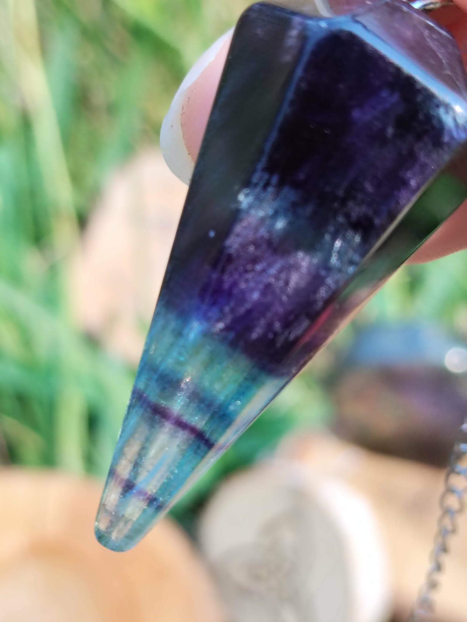 Gros plan sur pendule en fluorite facettée, dégradé violet/vert, décor végétal et bois, aide à la clarté mentale et au recentrage