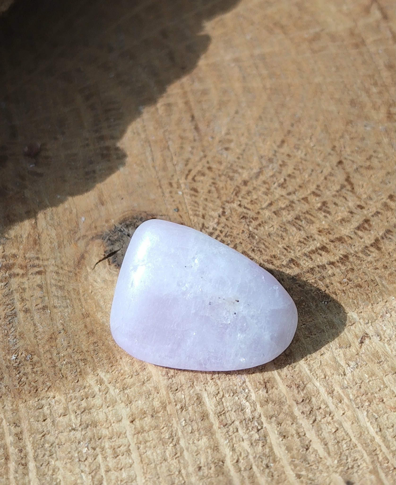 Pierre roulée de kunzite rose très pâle, galet poli de forme triangulaire posé sur rondin de bois clair, pierre naturelle liée à la douceur du cœur, à la tranquillité et au recentrage.