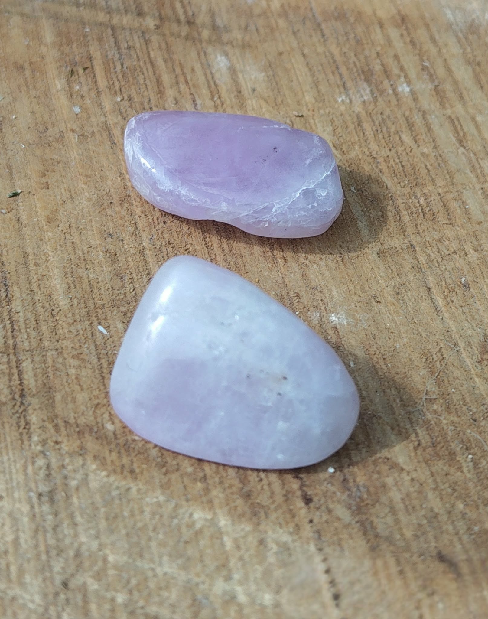 Pierre roulée de kunzite rose pâle à lilas, polie et lisse, posée sur planche en bois, galet naturel relié à la paix émotionnelle, à la délicatesse et à l’harmonie du cœur.