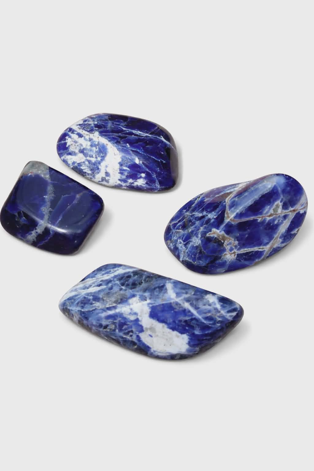 Pierre roulée de sodalite bleu profond veinée de blanc sur rondin de bois naturel, galet poli relié à la confiance tranquille, au calme intérieur et à l’expression sincère.