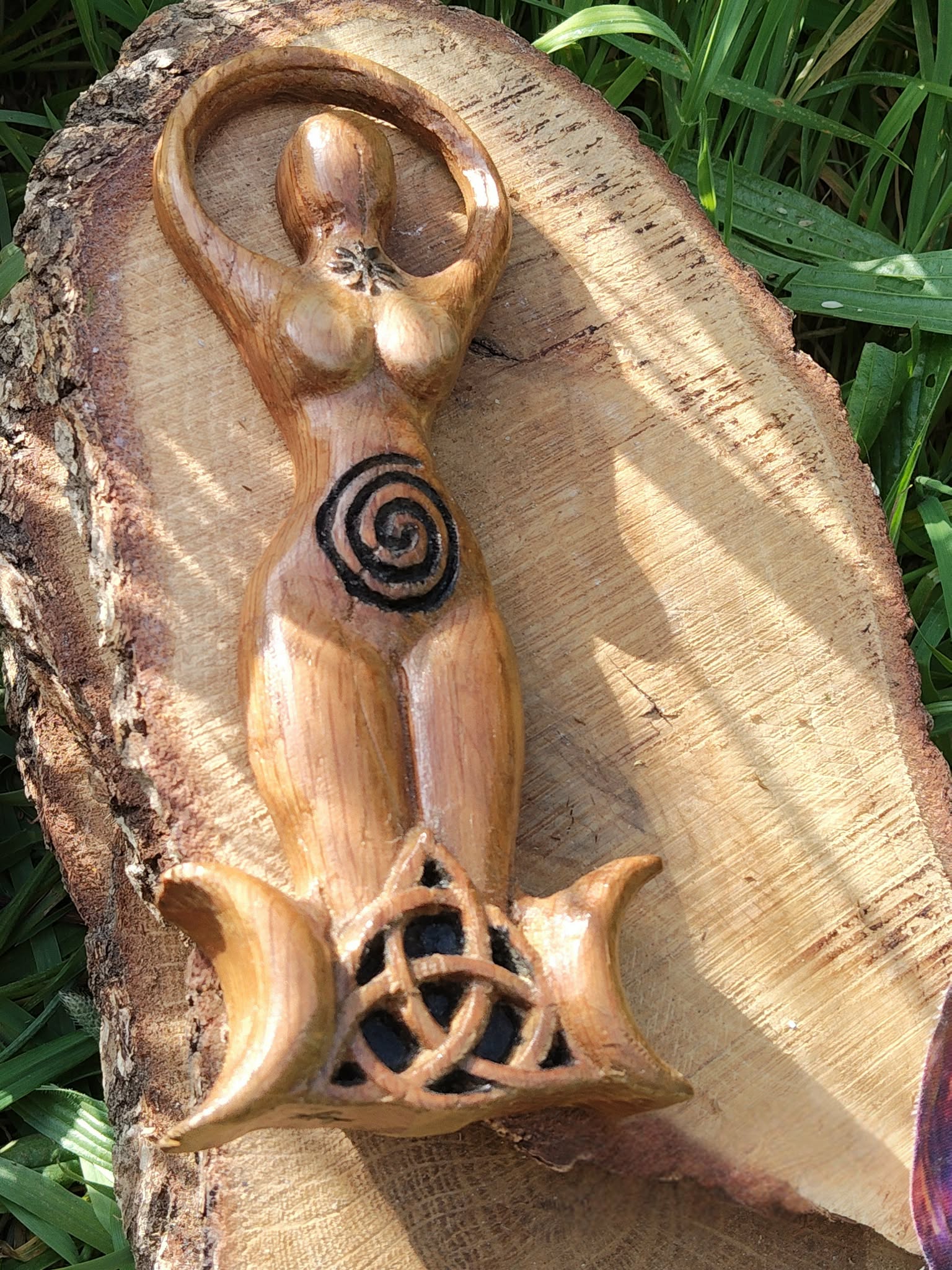 Statuette Gaïa (déesse) en bois style wicca avec spirale et triquetra, posée sur écorce dans un décor végétal; évoque ancrage, protection douce, harmonie, énergie féminine et intuition, idéale pour autel et déco ésotérique.