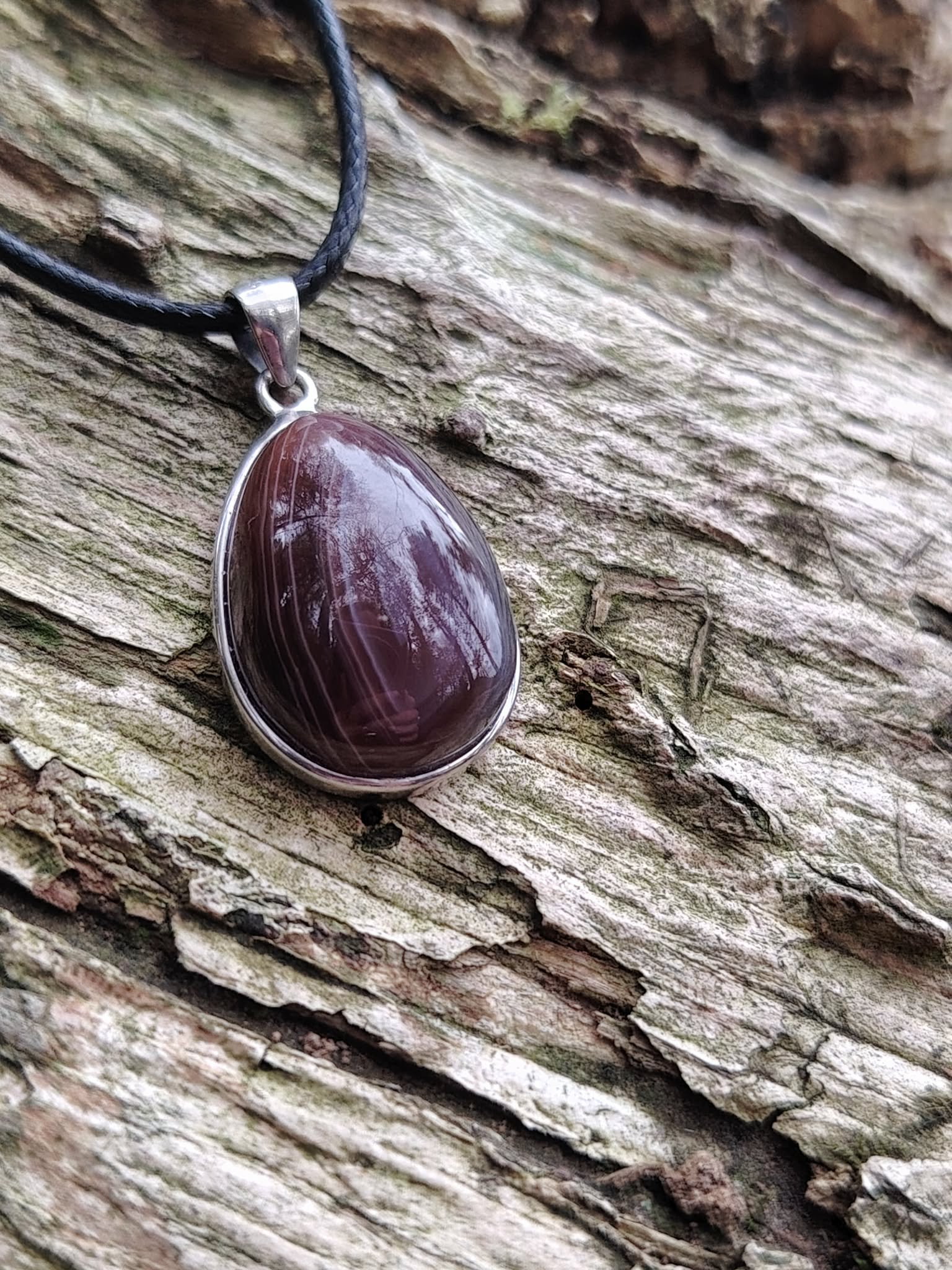 Pendentif agate du Botswana goutte polie à bandes brun-gris sur décor écorce et bois texturé, réassurance émotionnelle et ancrage paisible
