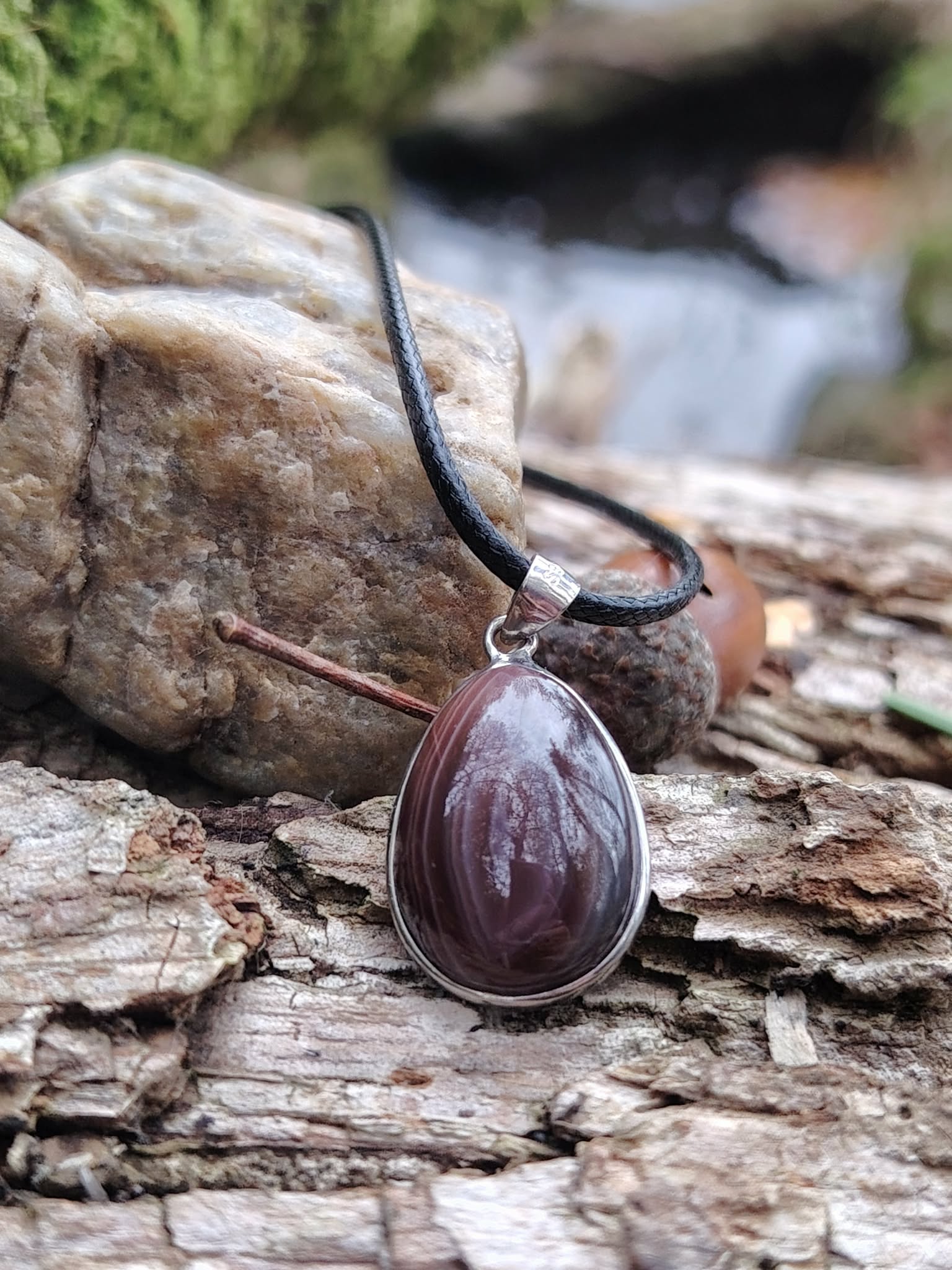 Pendentif agate du Botswana à stries naturelles gris-brun sur cordon noir, décor minéral sur écorce et roches, équilibre du ressenti et sérénité