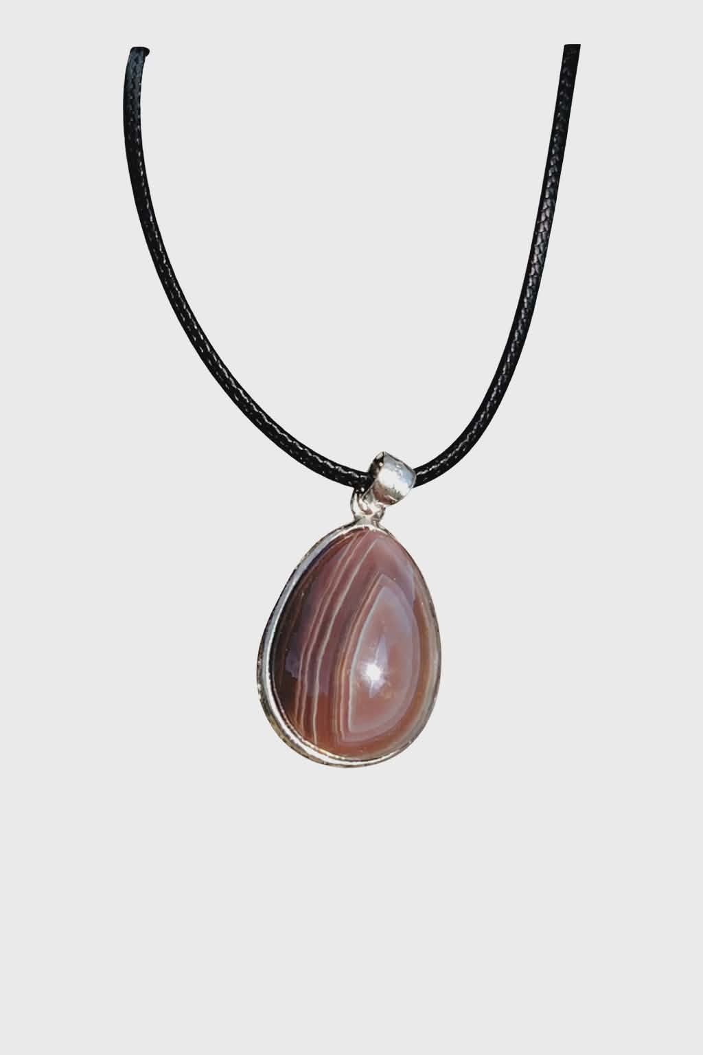 Pendentif agate du Botswana en goutte sur fond blanc, bandes brun-gris serties métal argenté, bijou sobre au style minéral apaisant