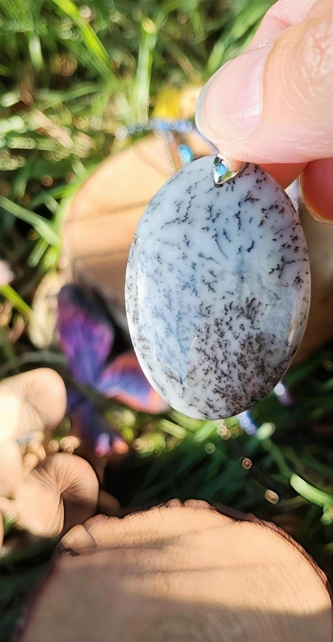 Pendentif opale dendritique ovale en extérieur parmi feuilles vertes et bois, bijou naturel pour calme du mental et intuition posée