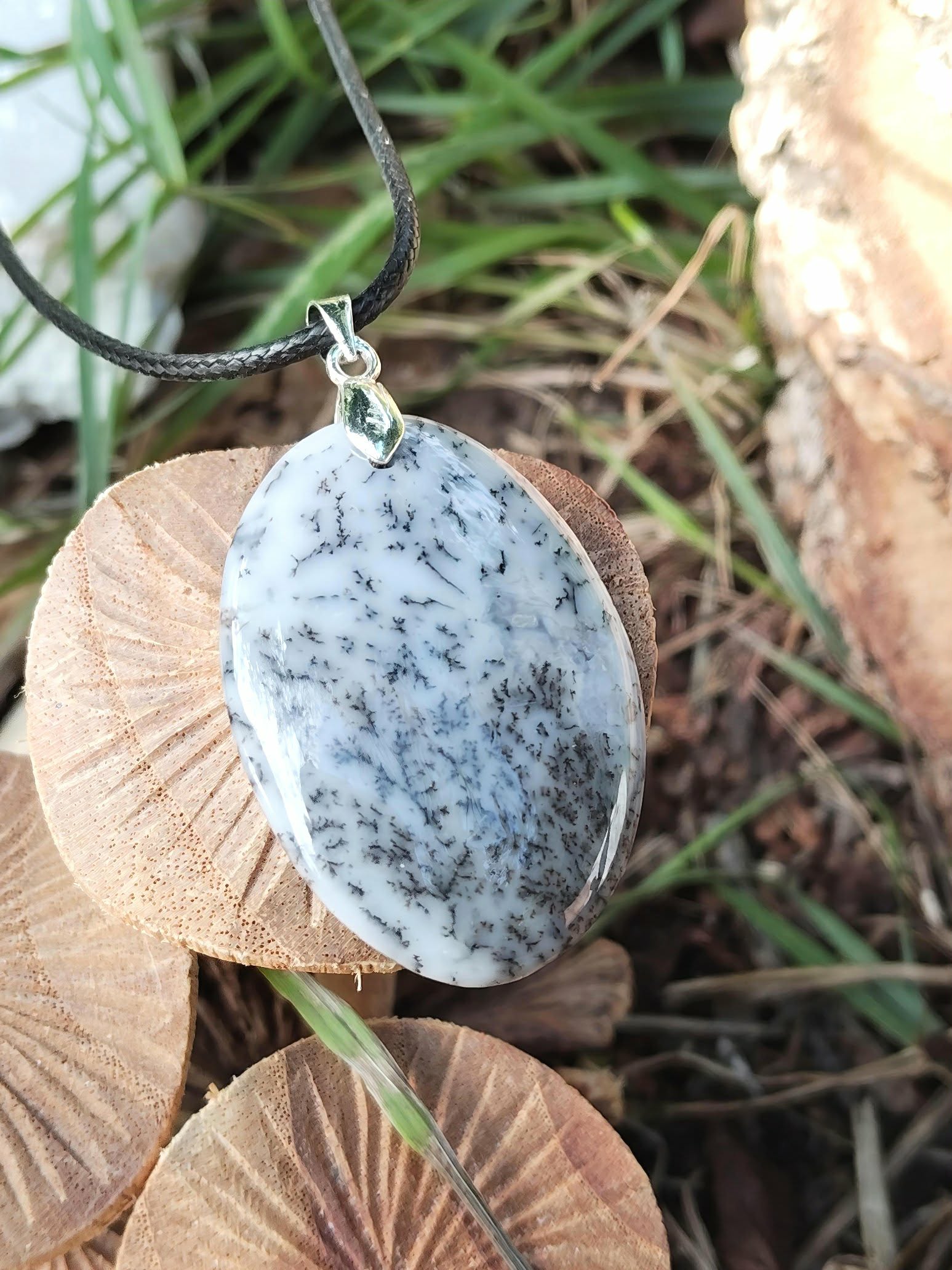 Pendentif opale dendritique ovale sur cordon noir, photographié en forêt sur bois en Bretagne, recentrage intérieur et présence apaisée