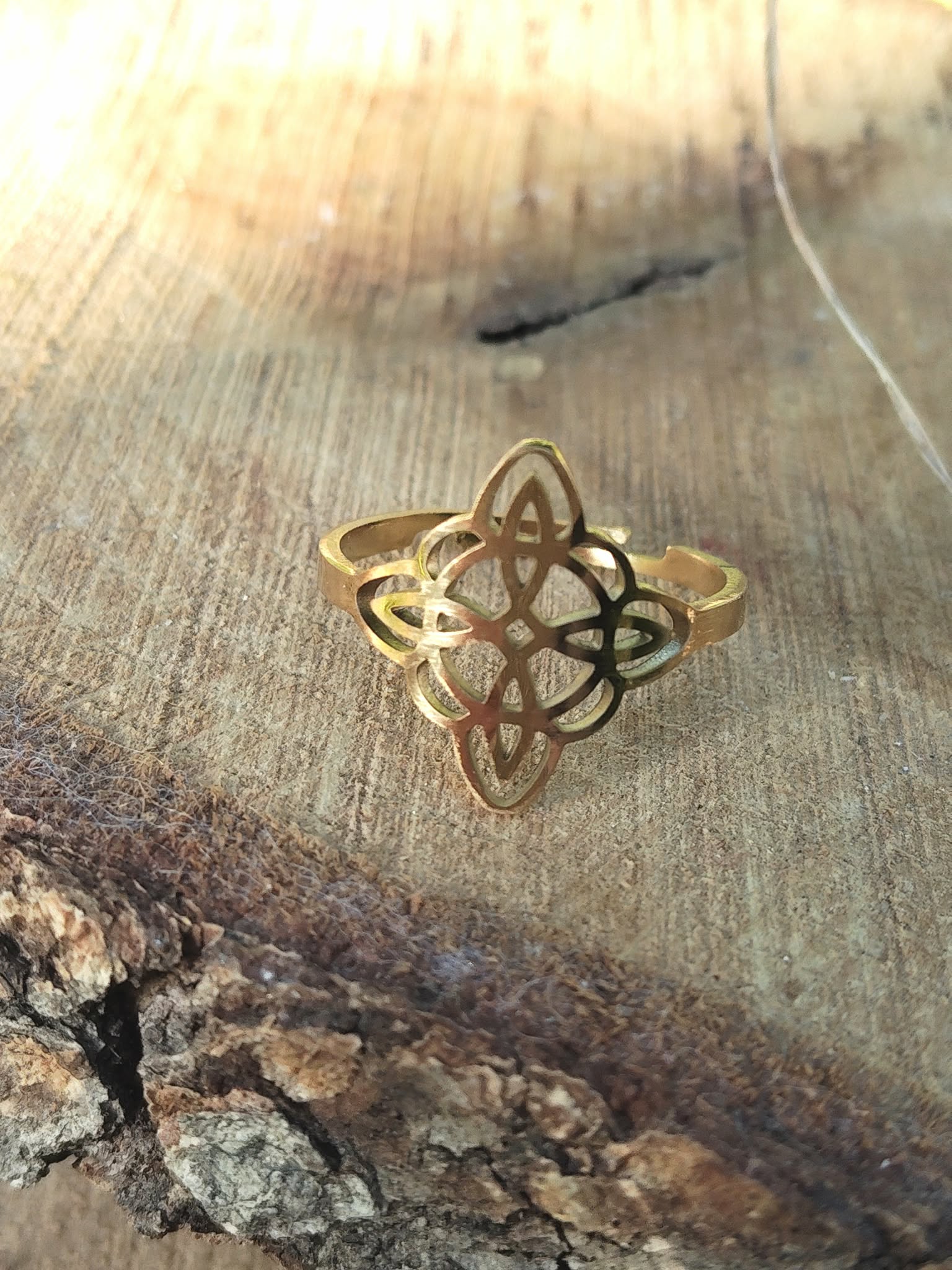 Bague réglable en acier inoxydable doré, motif nœud de sorcière, sur bois rustique; symbole de force intérieure.