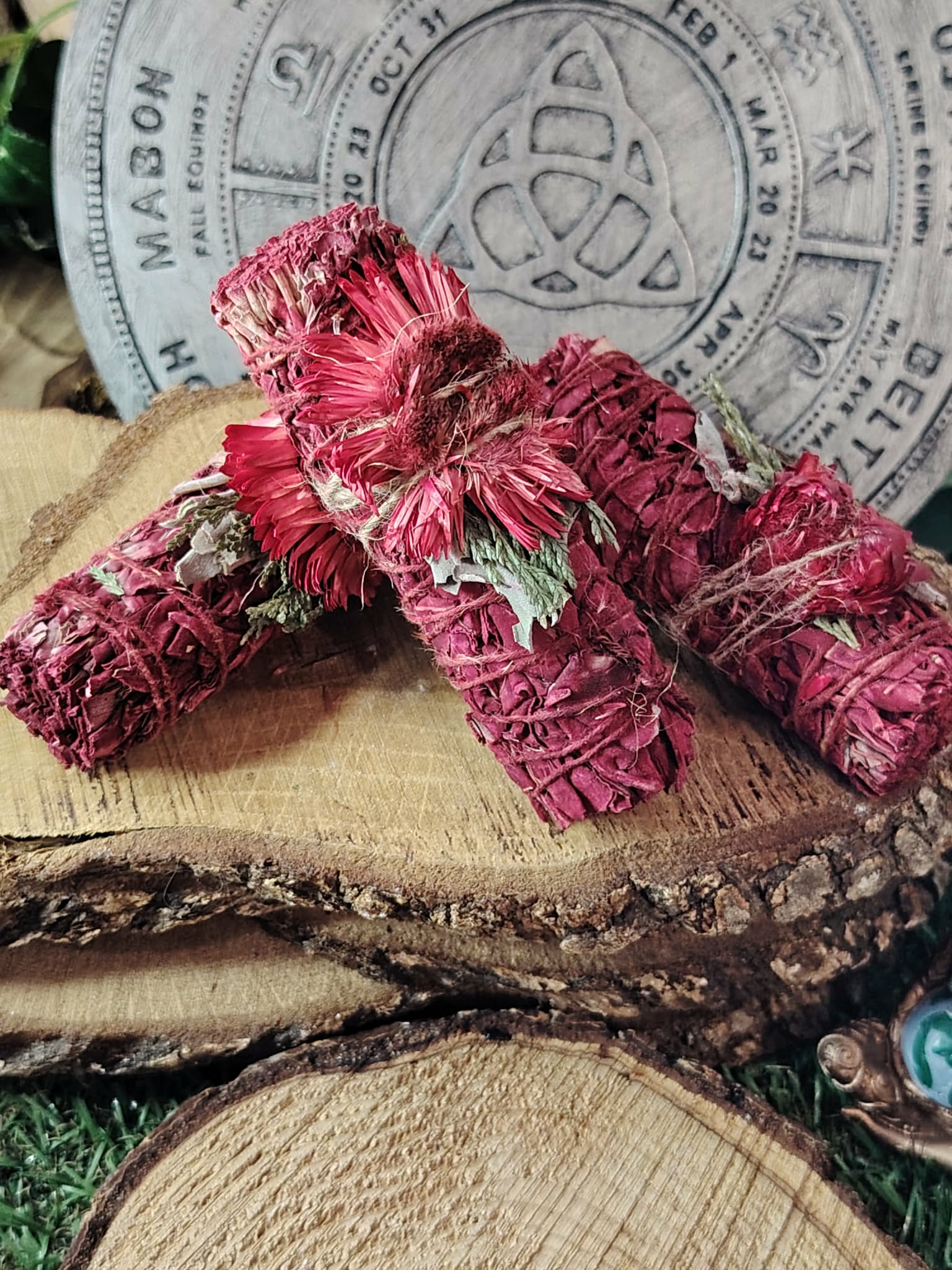 Bâtons de fumigation sauge blanche “sang de dragon”, fagots rouges avec fleurs séchées, posés sur rondins de bois, décor ésotérique en arrière-plan; pour purifier l’ambiance et poser une intention de protection.