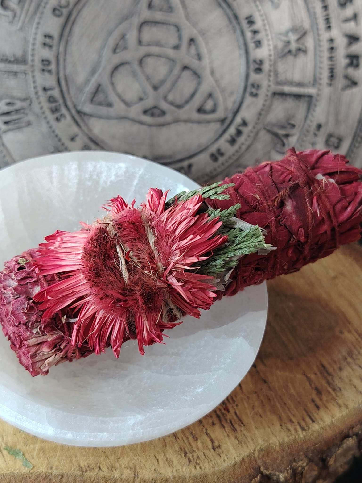 Bâton de fumigation sauge blanche “sang de dragon”, fleurs séchées rouges/roses, posé sur coupelle blanche et rondin de bois, fond ésotérique; pour purifier l’ambiance et poser une intention de protection