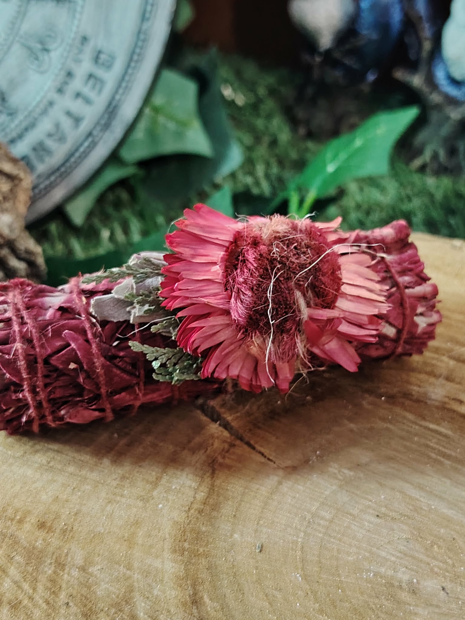 Smudge stick sauge   sang de dragon, fagot rouge ligoté, fleurs séchées, photo sur tranche de bois avec fond vert; idéal pour nettoyage énergétique, recentrage et clarté.