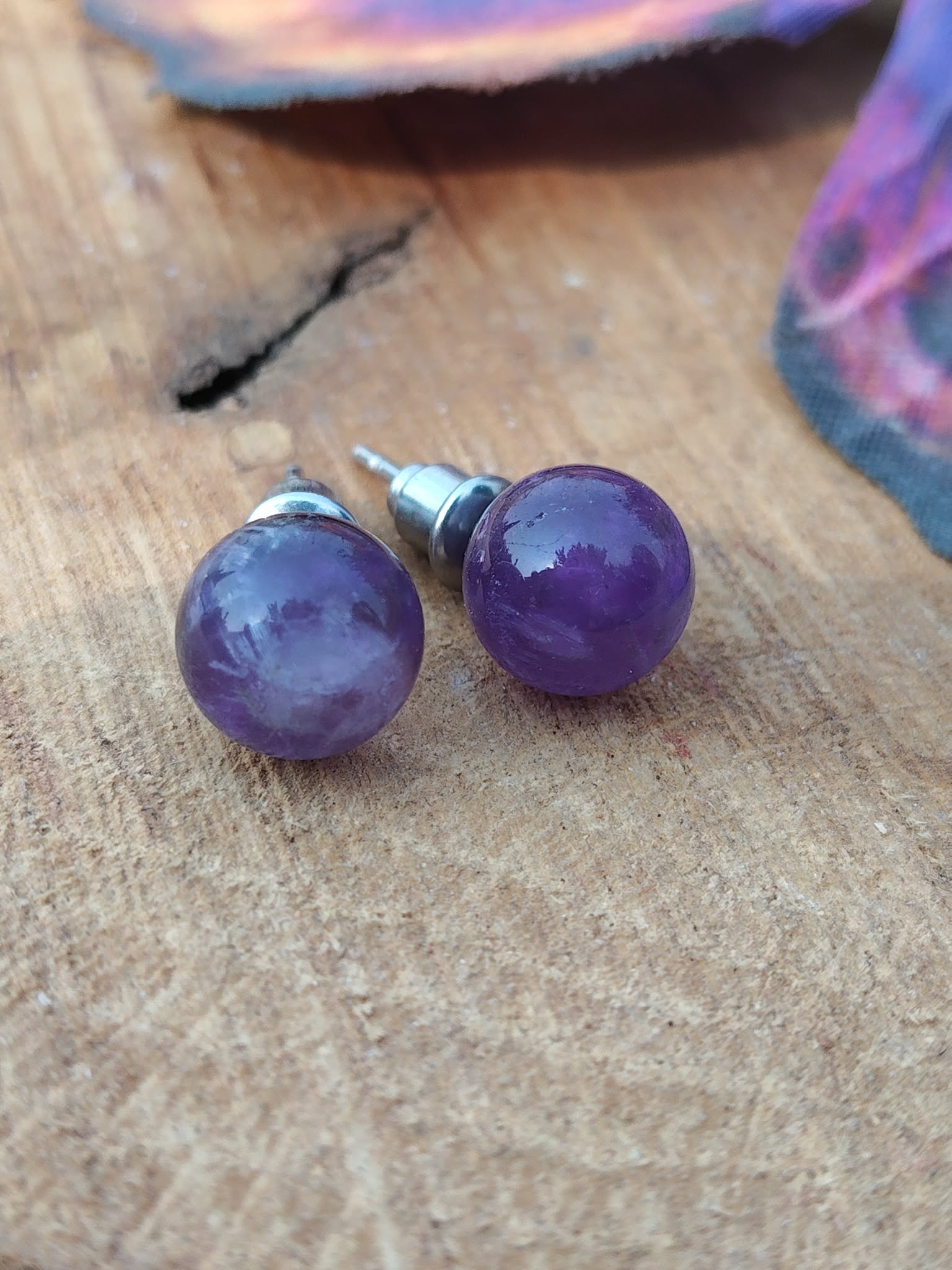 Boucles d’oreilles puces améthyste violettes en inox 304 sur planche en bois, mise au point sur les perles, fond doux et flouté; associée à sérénité, équilibre émotionnel, intuition.