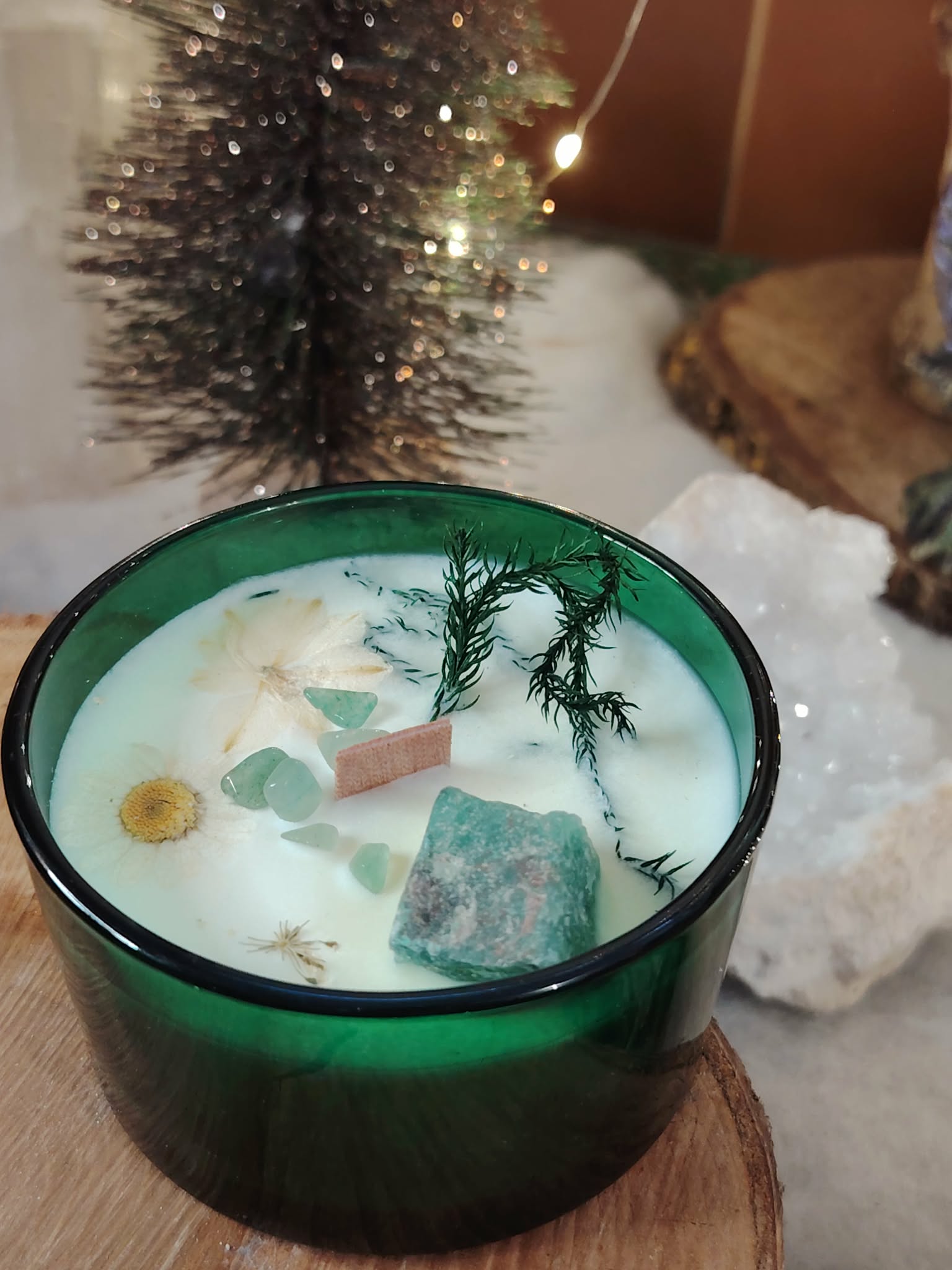 Bougie jade menthe-citron en cire de soja, pot en verre vert, mèche en bois, éclats de jade et fleurs séchées; décor hivernal avec sapin lumineux et cristaux.