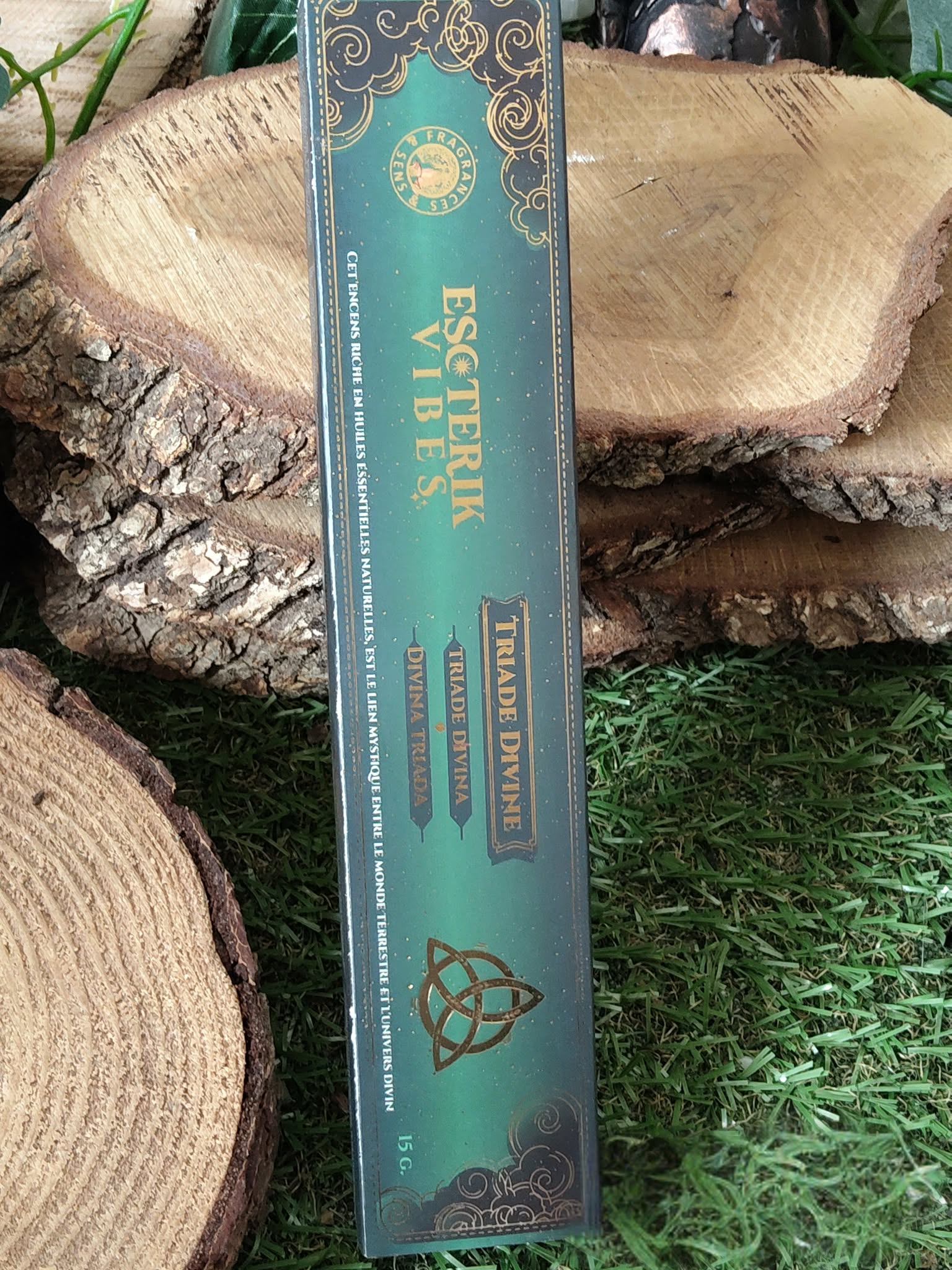 Encens Esoteric Vibes triquetra en étui turquoise à motifs celtiques, posé entre rondins de bois et mousse verte; inspire protection, harmonie, apaisement et ancrage.