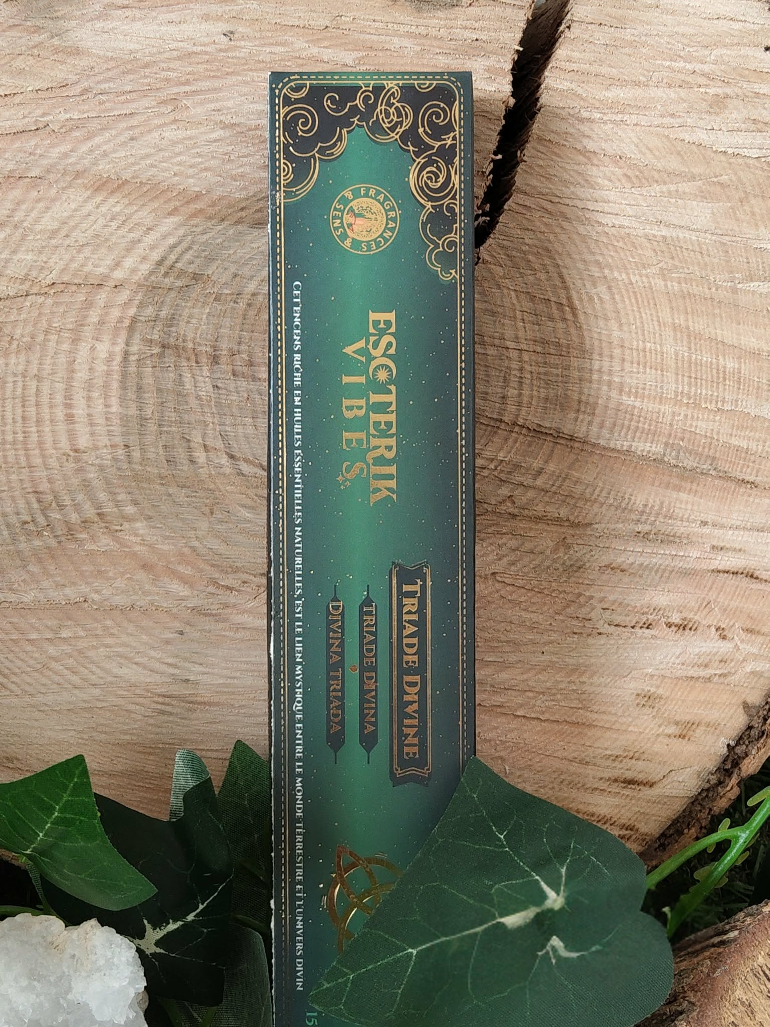 Encens Esoteric Vibes triquetra présenté verticalement sur fond bois naturel (anneaux visibles) avec feuillage; soutient calme intérieur, équilibre émotionnel et ancrage.