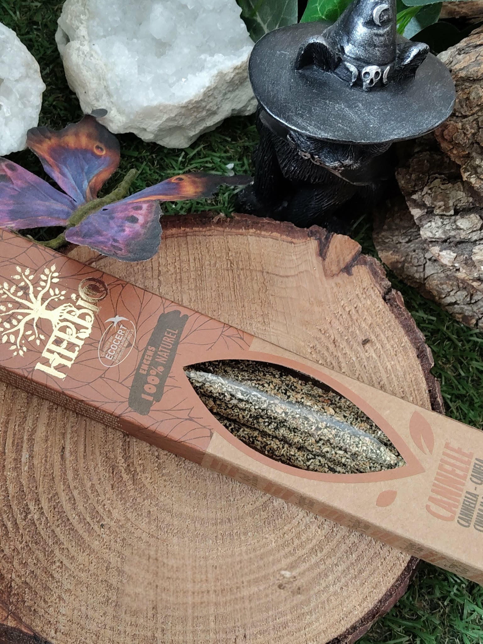Encens HERBIO Cannelle 25 g en étui kraft couché sur tranche de bois, décor nature avec cristaux et petite figurine sur socle noir; senteur épicée, atmosphère cosy et apaisante.