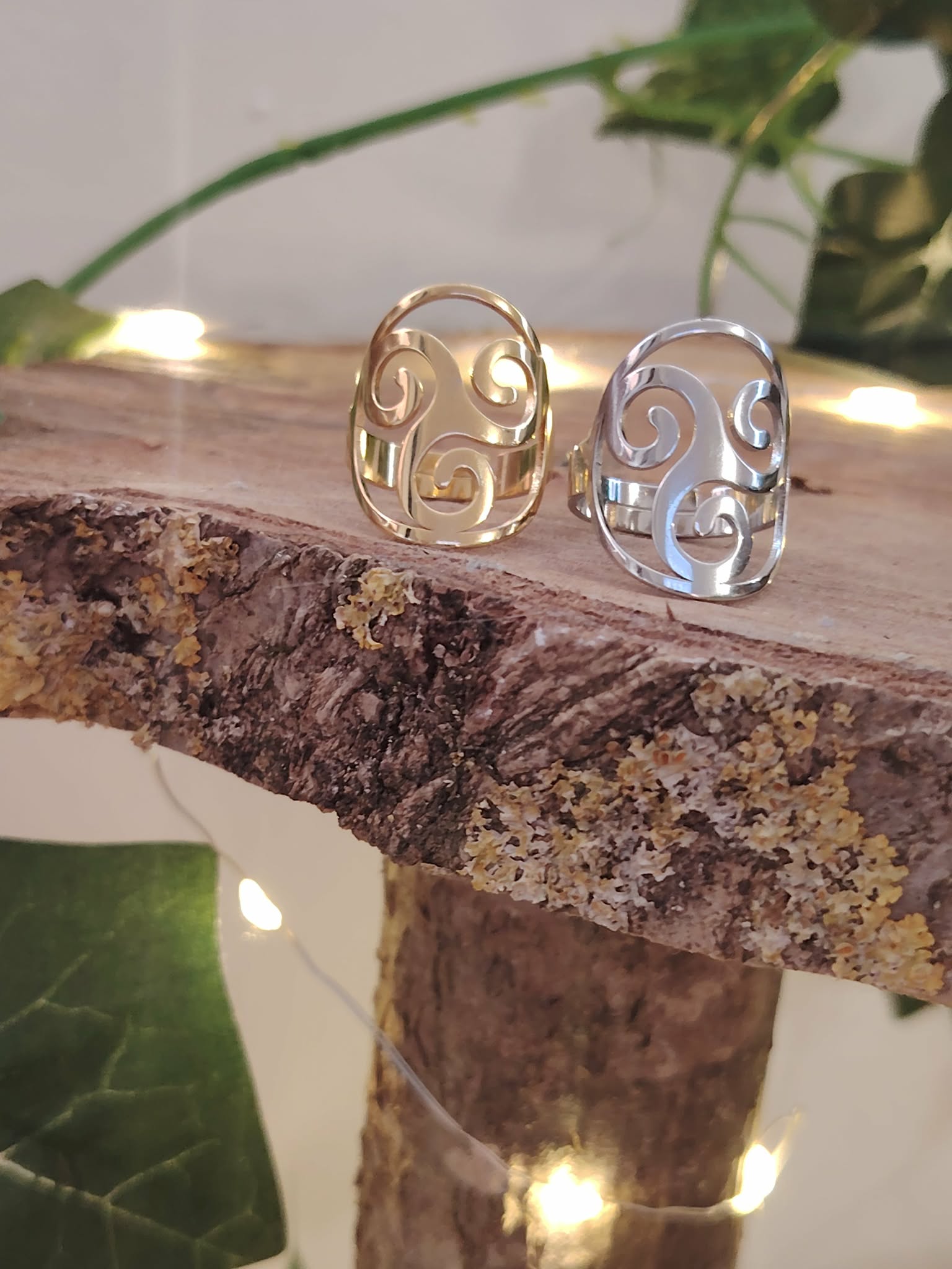 Deux bagues Triskell inox doré et argenté posées sur branche, décor feuillage; symbole cycles et équilibre.