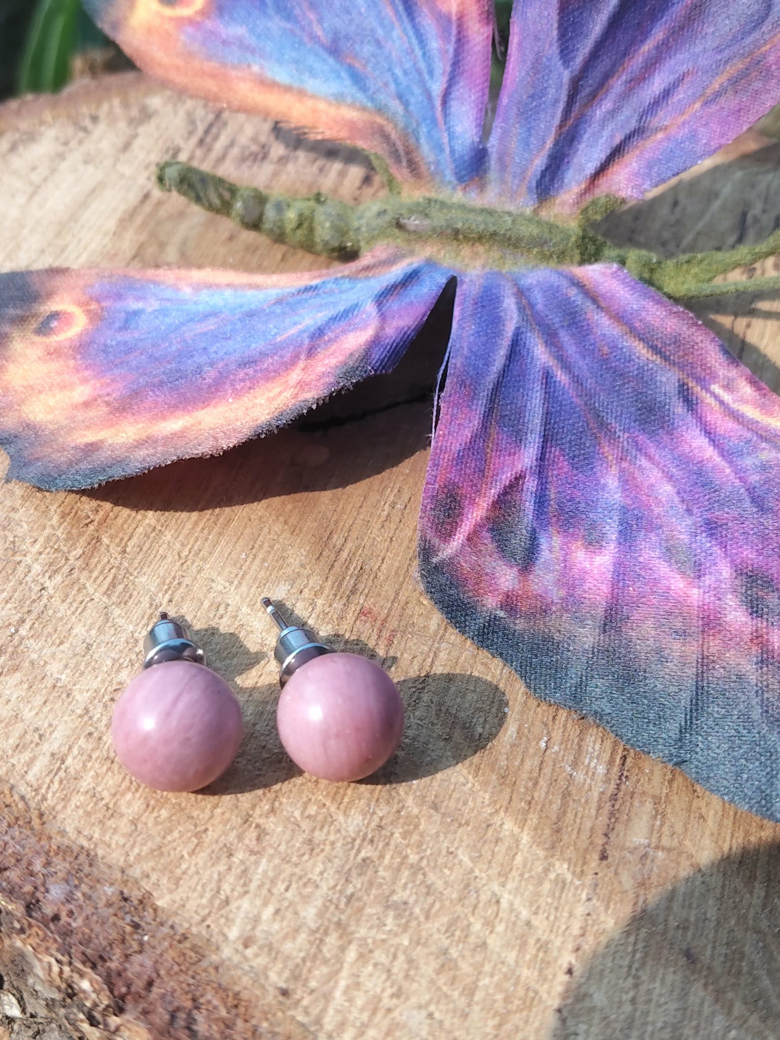 Boucles d’oreilles puces rhodonite rose, tiges acier inoxydable, sur tranche de bois avec papillon bleu/violet; douceur, apaisement émotionnel.