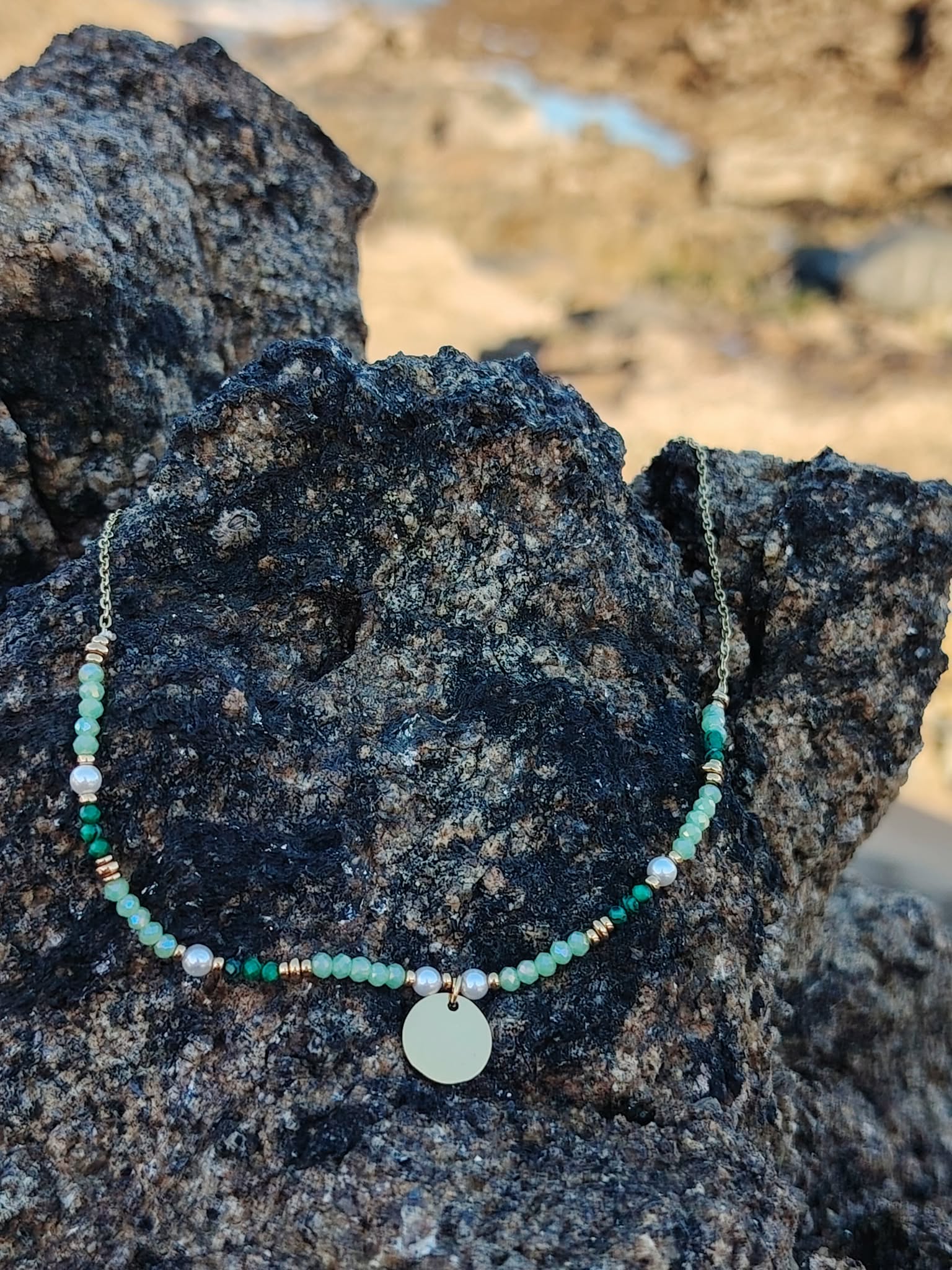 Collier en acier inoxydable doré orné de cristaux verts et petites perles sur rochers près de l’océan, bijou raffiné au charme frais