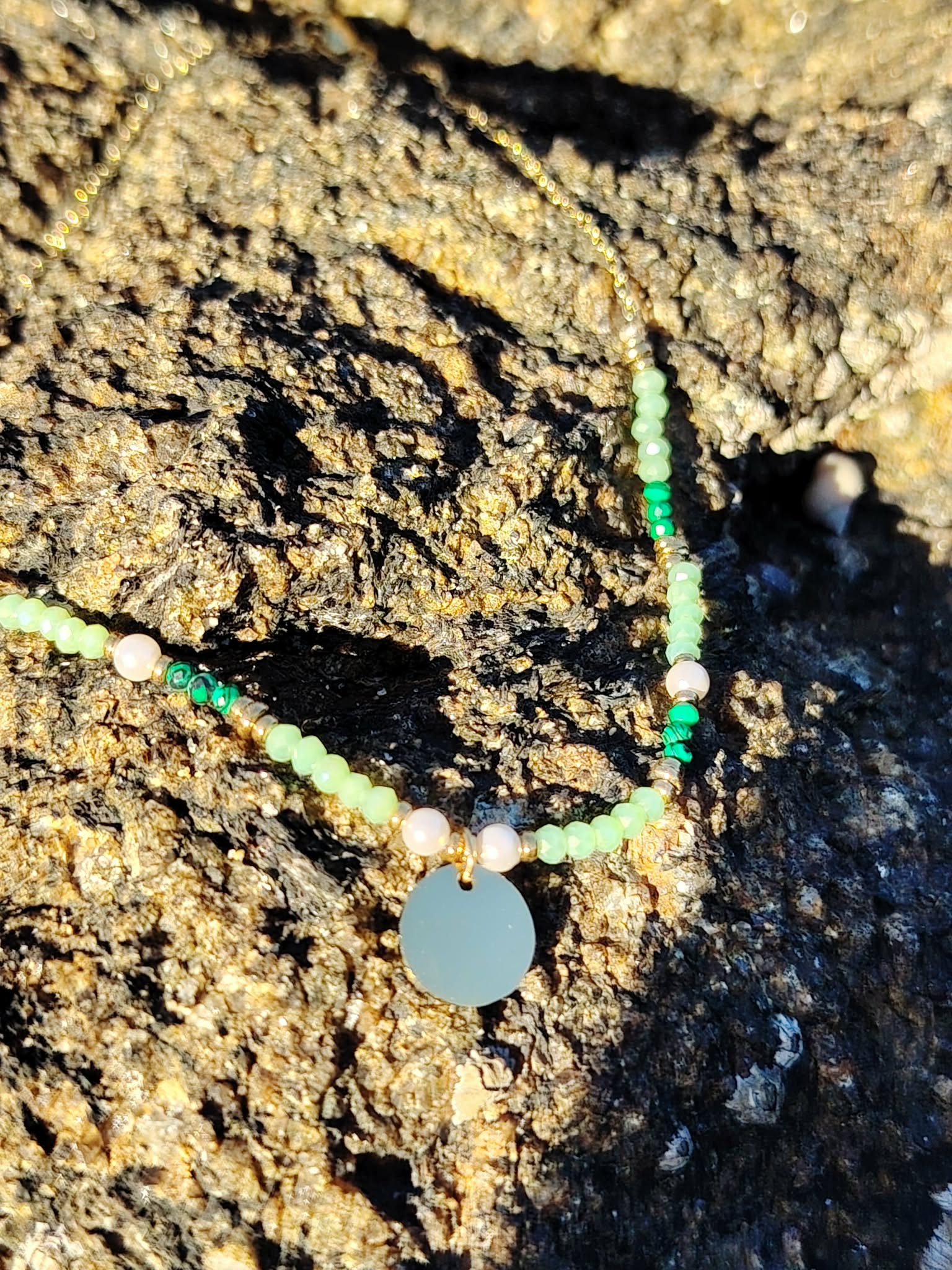 Collier doré avec cristaux verts et pendentif rond photographié sur une tranche de bois en Bretagne, esprit nature et élégance douce