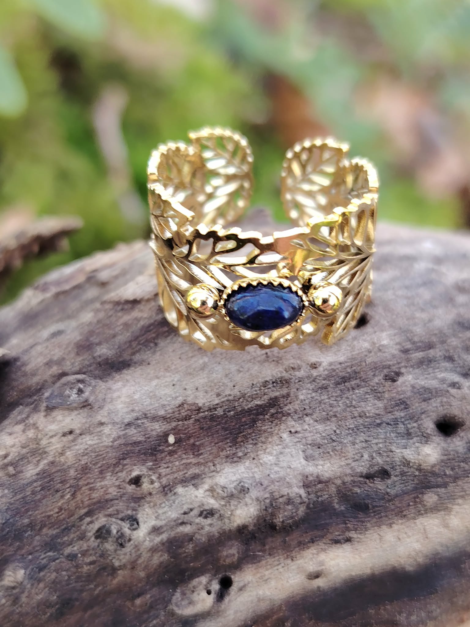 Bague dorée réglable en acier inoxydable, motif feuilles et pierre ovale lapis-lazuli, photographiée en Bretagne sur bois.