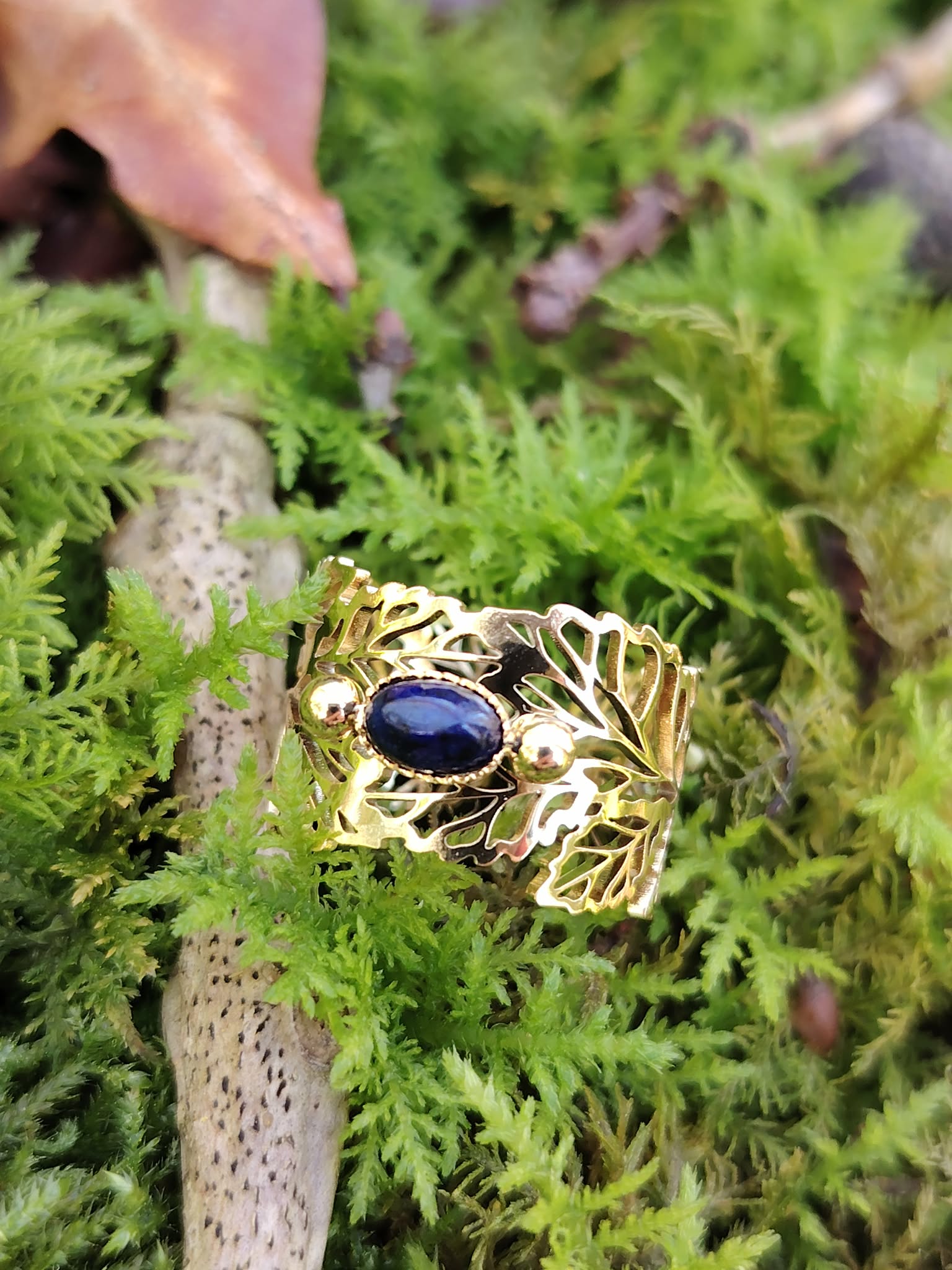 Bague dorée réglable en acier inoxydable, motif feuilles et pierre ovale lapis-lazuli, photo en Bretagne sur mousse et brindilles.