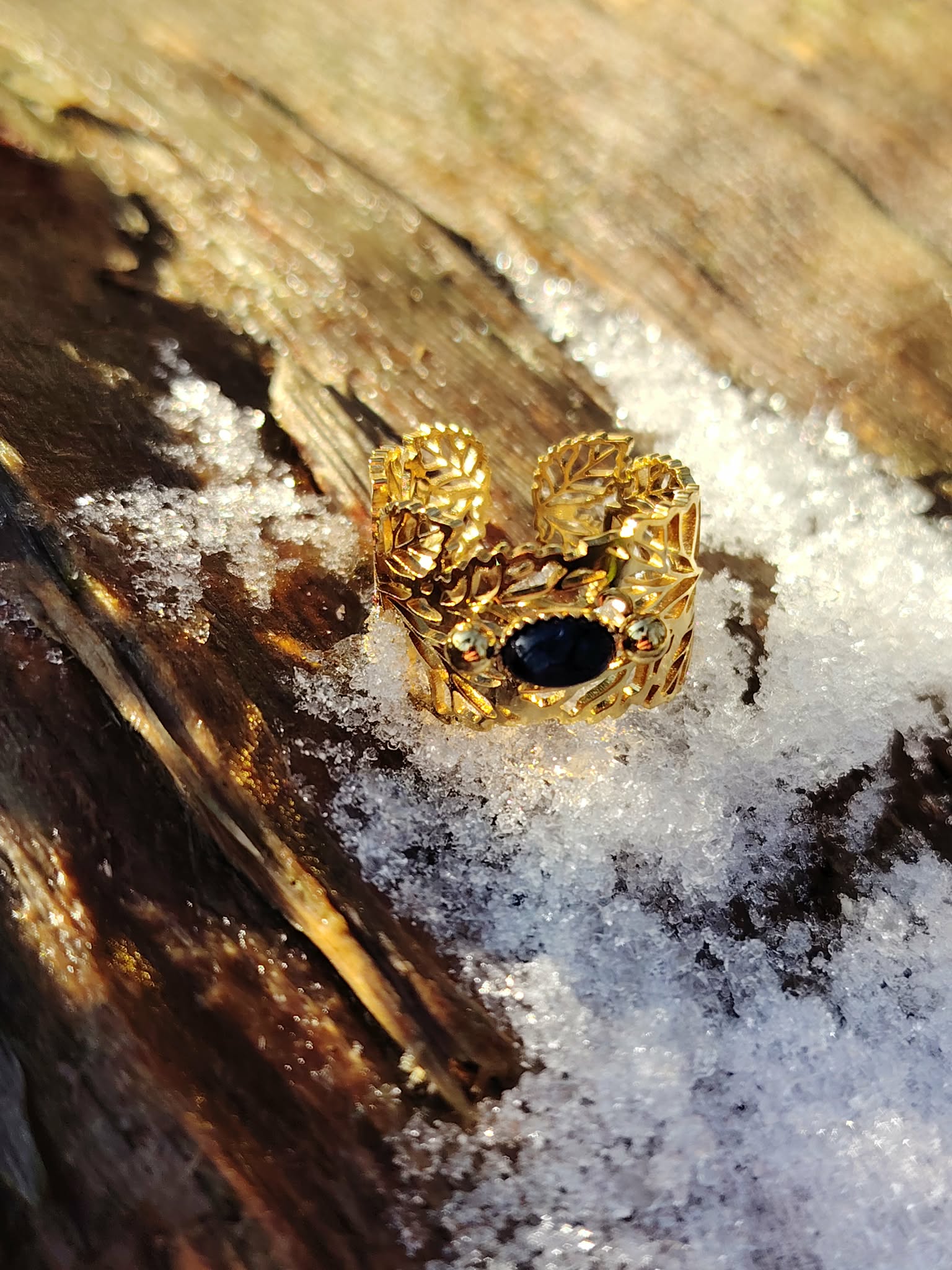 Bague dorée réglable en acier inoxydable, motif feuilles et pierre ovale lapis-lazuli, posée sur du bois avec neige fondue; photo en Bretagne.