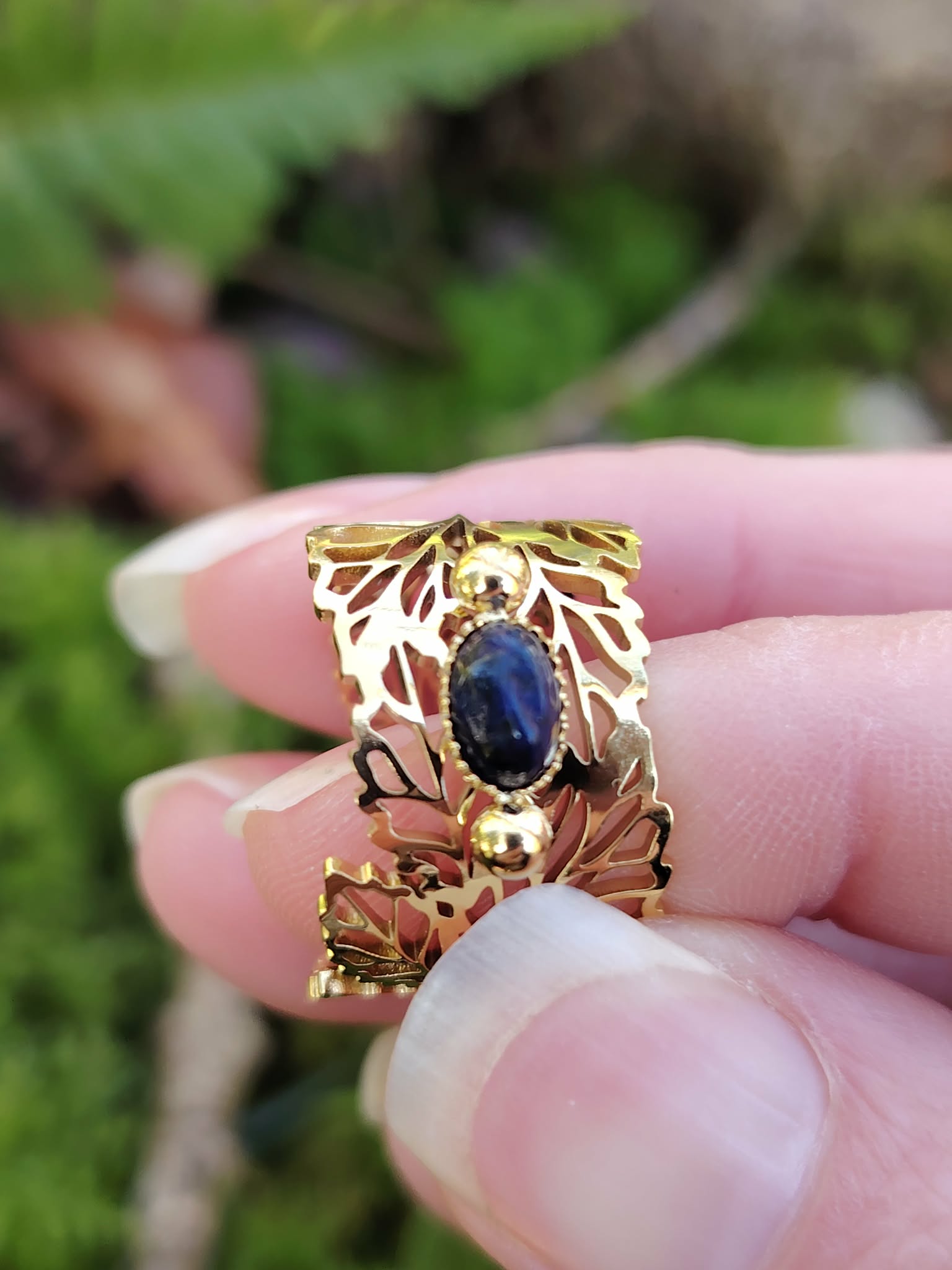Bague dorée réglable en acier inoxydable, motif feuilles et pierre ovale lapis-lazuli, tenue entre les doigts; photo en Bretagne.