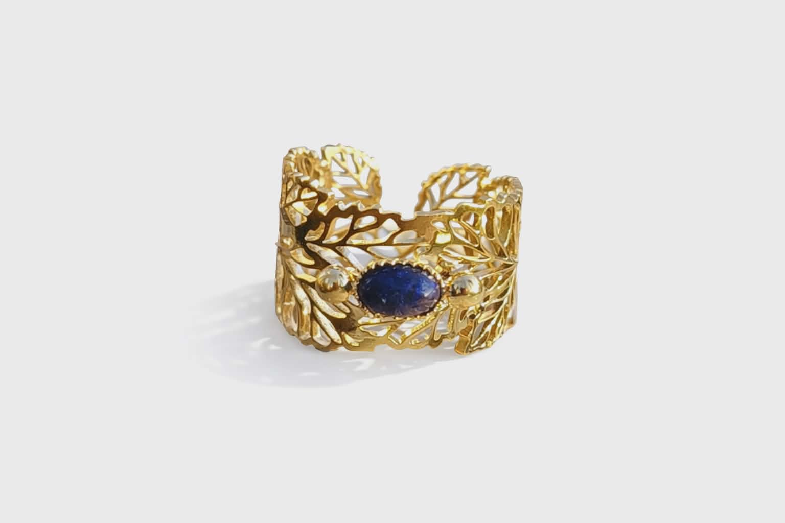 Bague dorée réglable en acier inoxydable, motif feuilles et pierre ovale lapis-lazuli, photographiée sur fond clair.