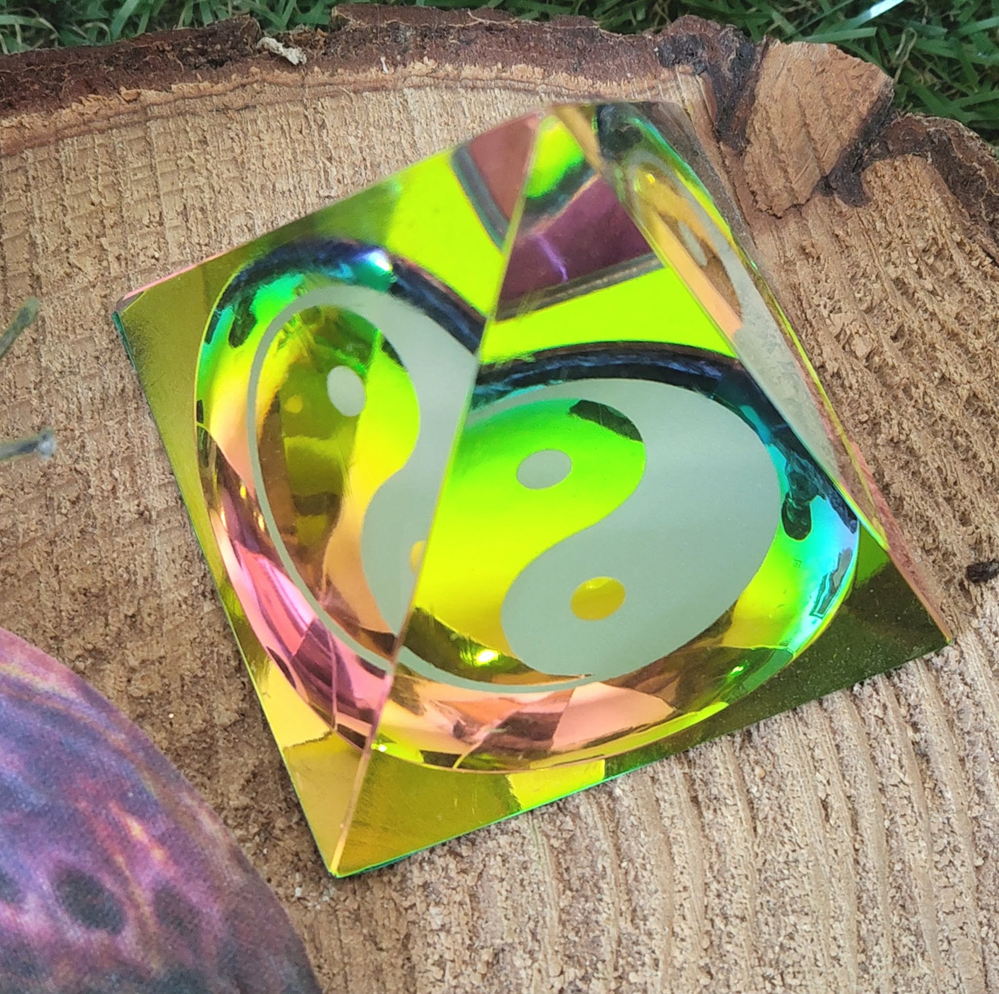 Pyramide décorative en cristal irisé vert-jaune avec symbole yin et yang, posée sur un support en bois texturé ; favorise l’harmonisation des polarités, l’apaisement et une atmosphère zen.