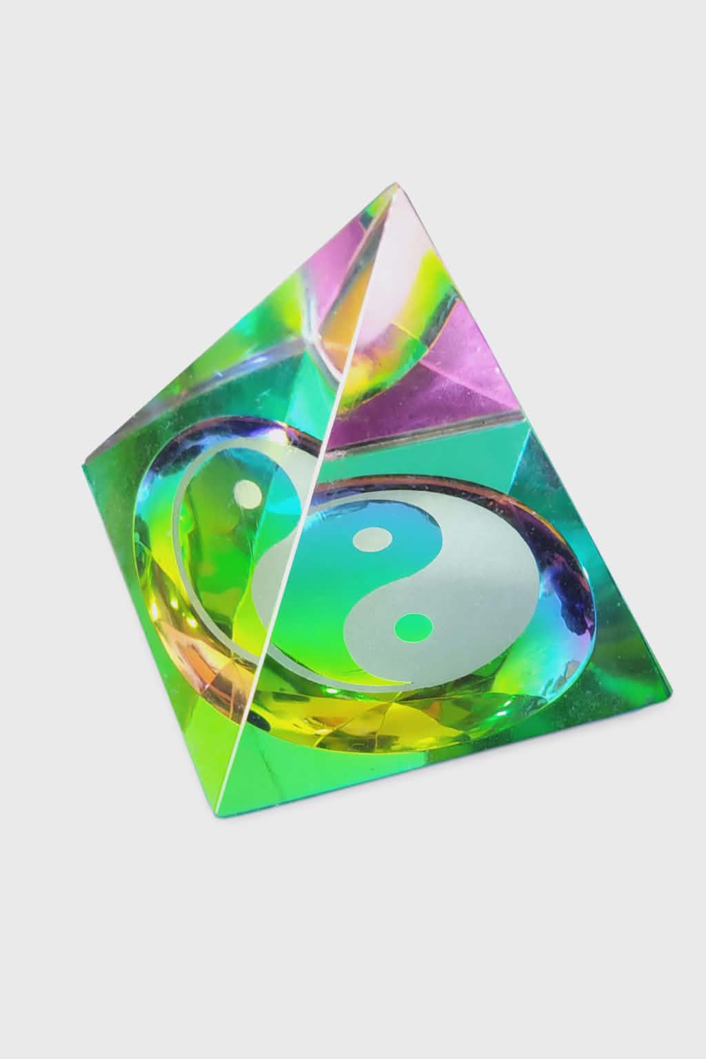 Pyramide en cristal irisé multicolore avec symbole yin et yang, photographiée sur fond blanc ; évoque l’équilibre, l’harmonie et l’apaisement.