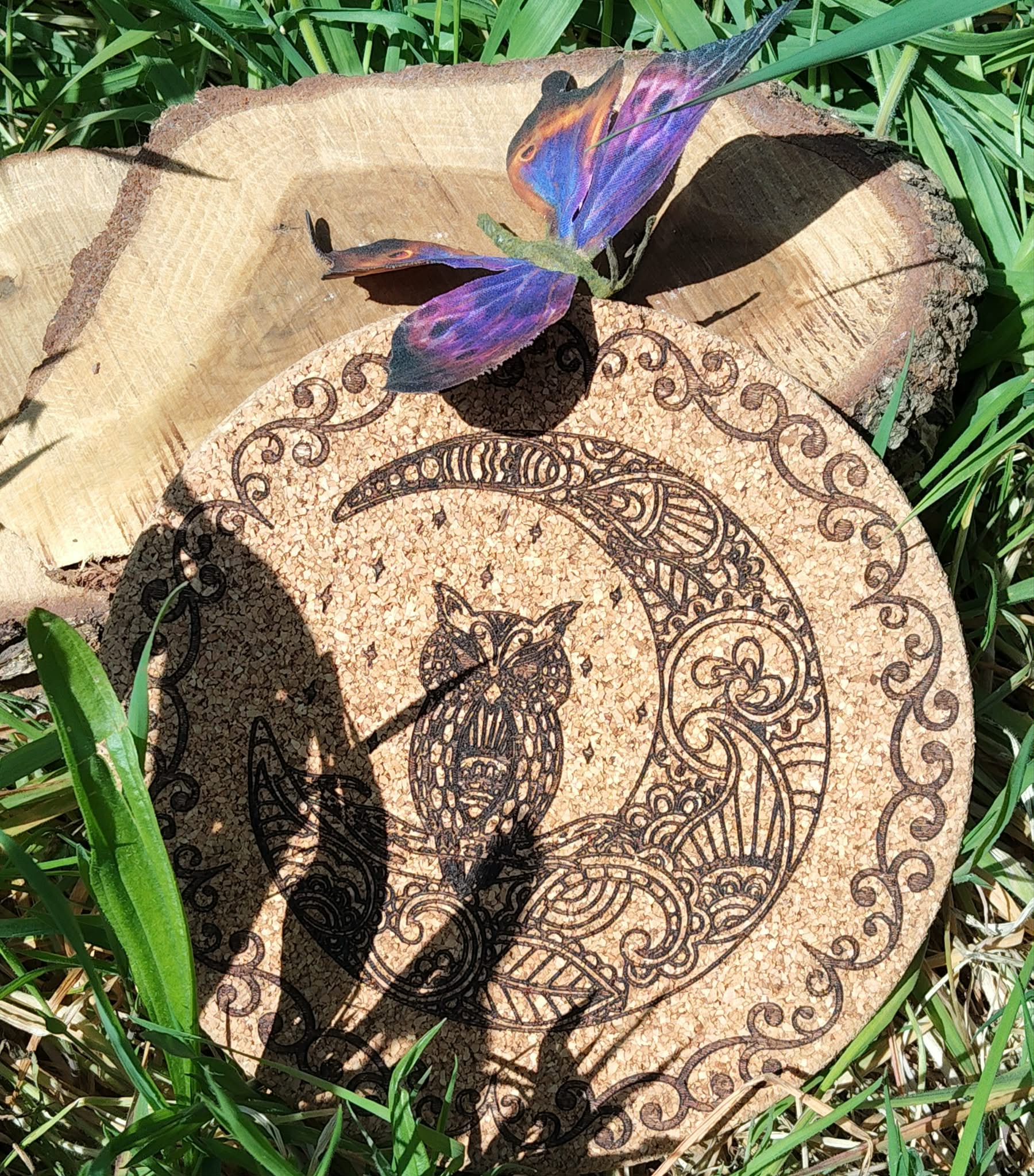 Dessous de plat rond en liège gravé d’une tête de loup avec arabesques, cercle décoratif et bordure celtique; photo dans l’herbe, papillon violet.