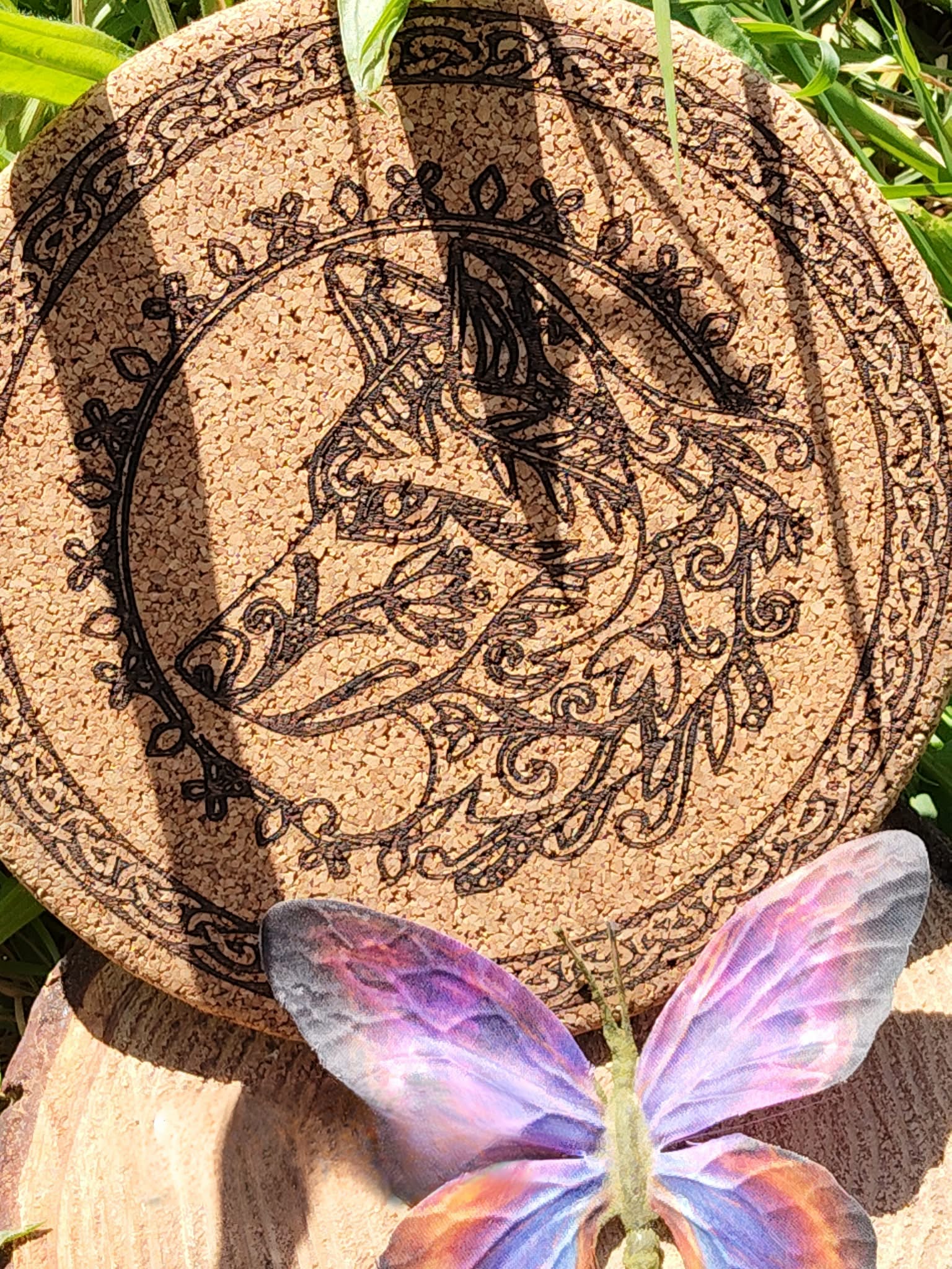 Dessous de plat rond en liège gravé symbole Om au centre, entouré d’un mandala et motifs géométriques; photo en extérieur dans l’herbe.