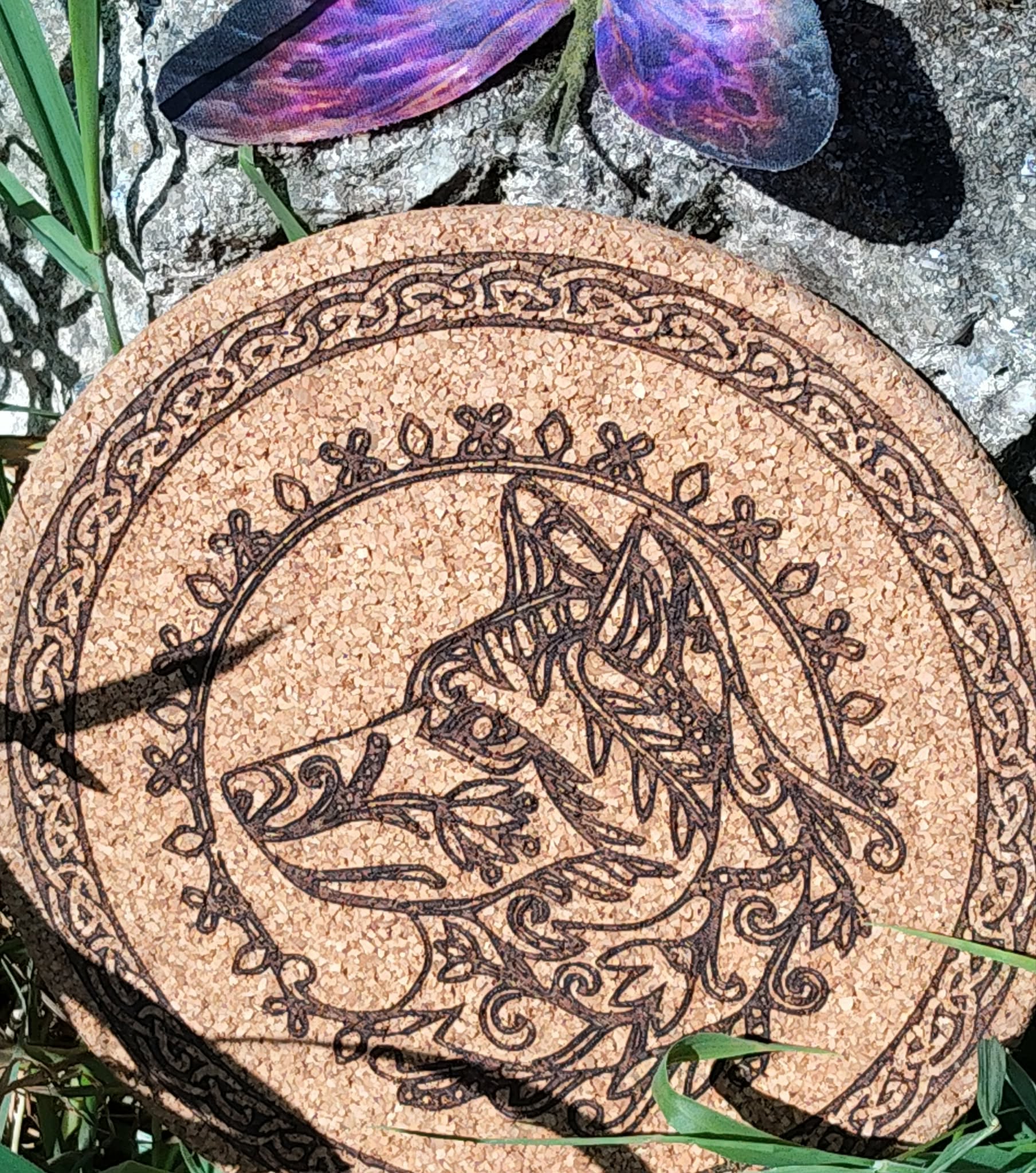 Dessous de plat rond en liège, loup gravé, bordure celtique; photo dans l’herbe, ombres de feuilles. Symbolique: instinct, protection, loyauté