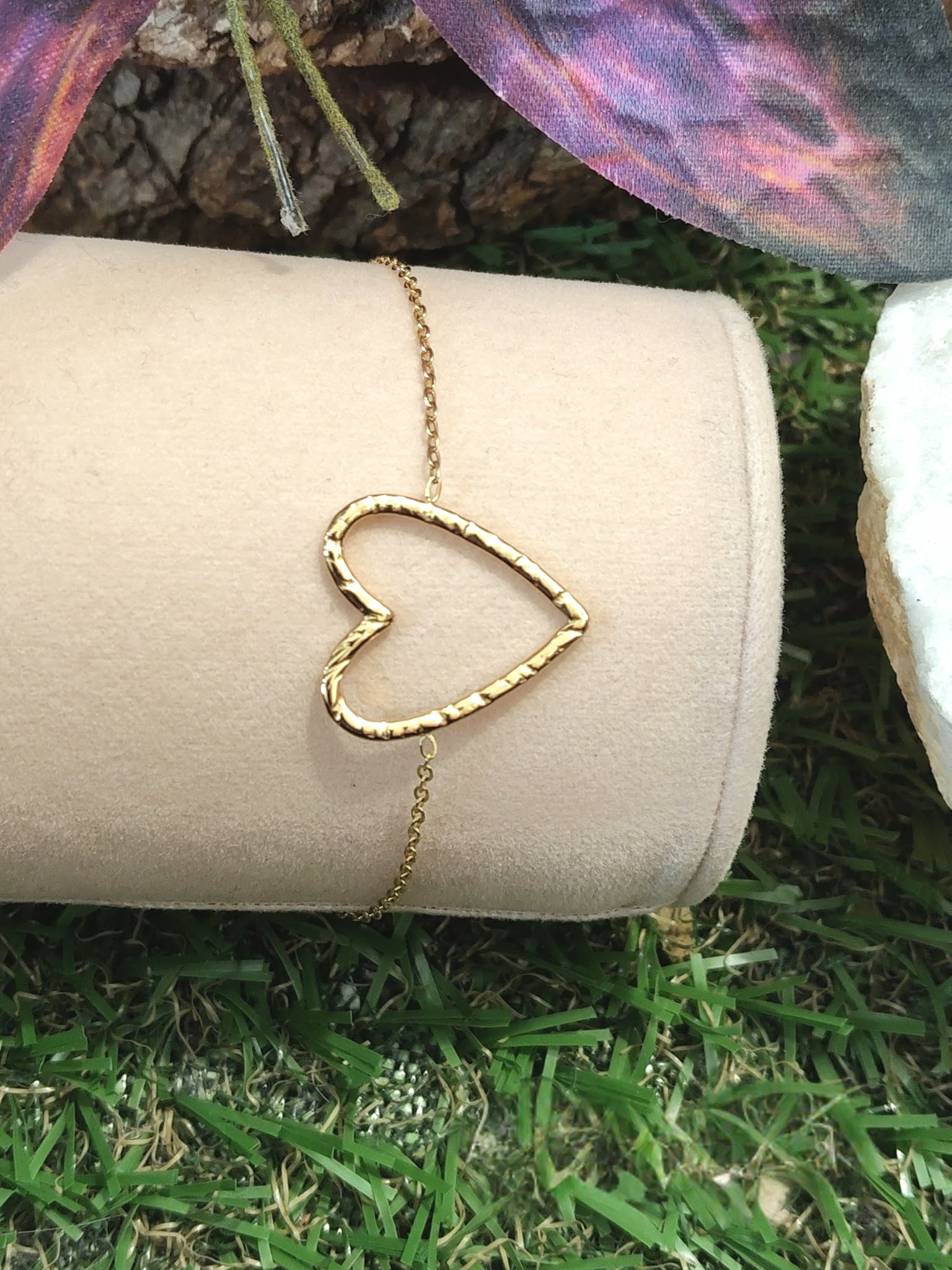 Bracelet chaîne fine en acier inoxydable doré, pendentif cœur ajouré; présenté sur support blanc, décor herbe et papillon violet en arrière-plan.