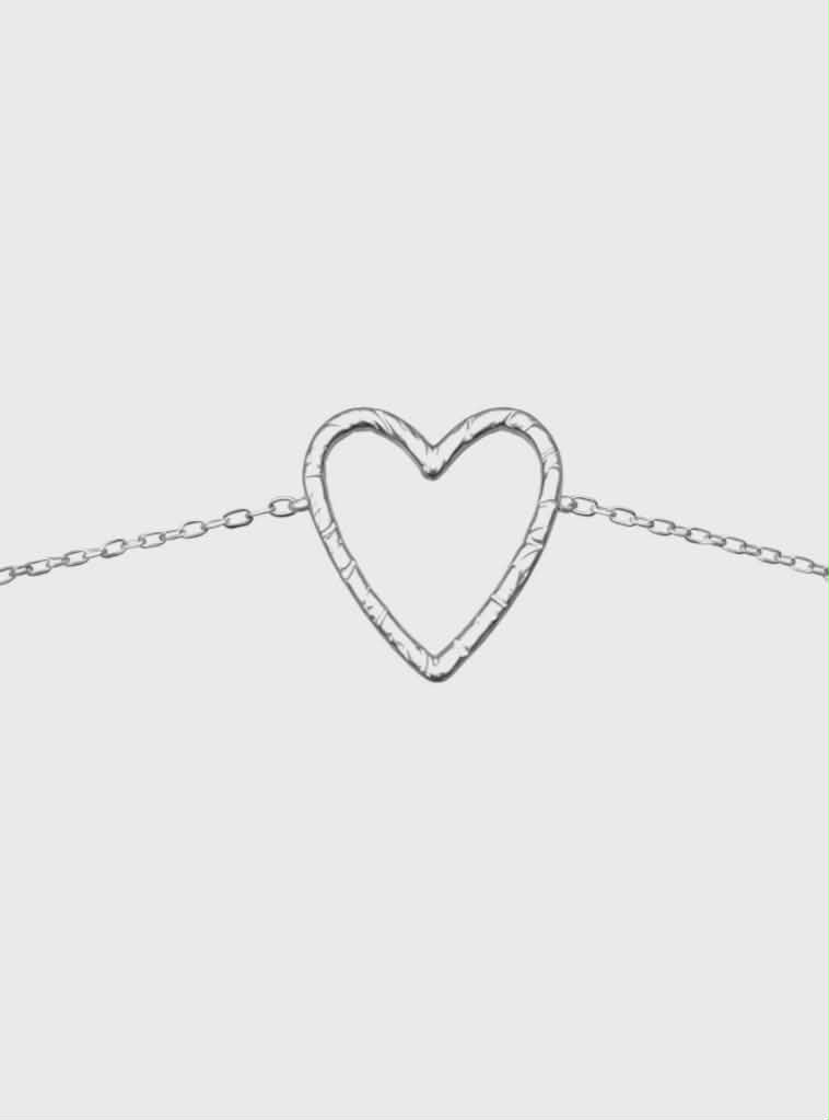 Bracelet chaîne fine en acier inoxydable argenté, pendentif cœur ajouré; photo produit sur fond blanc, centré.