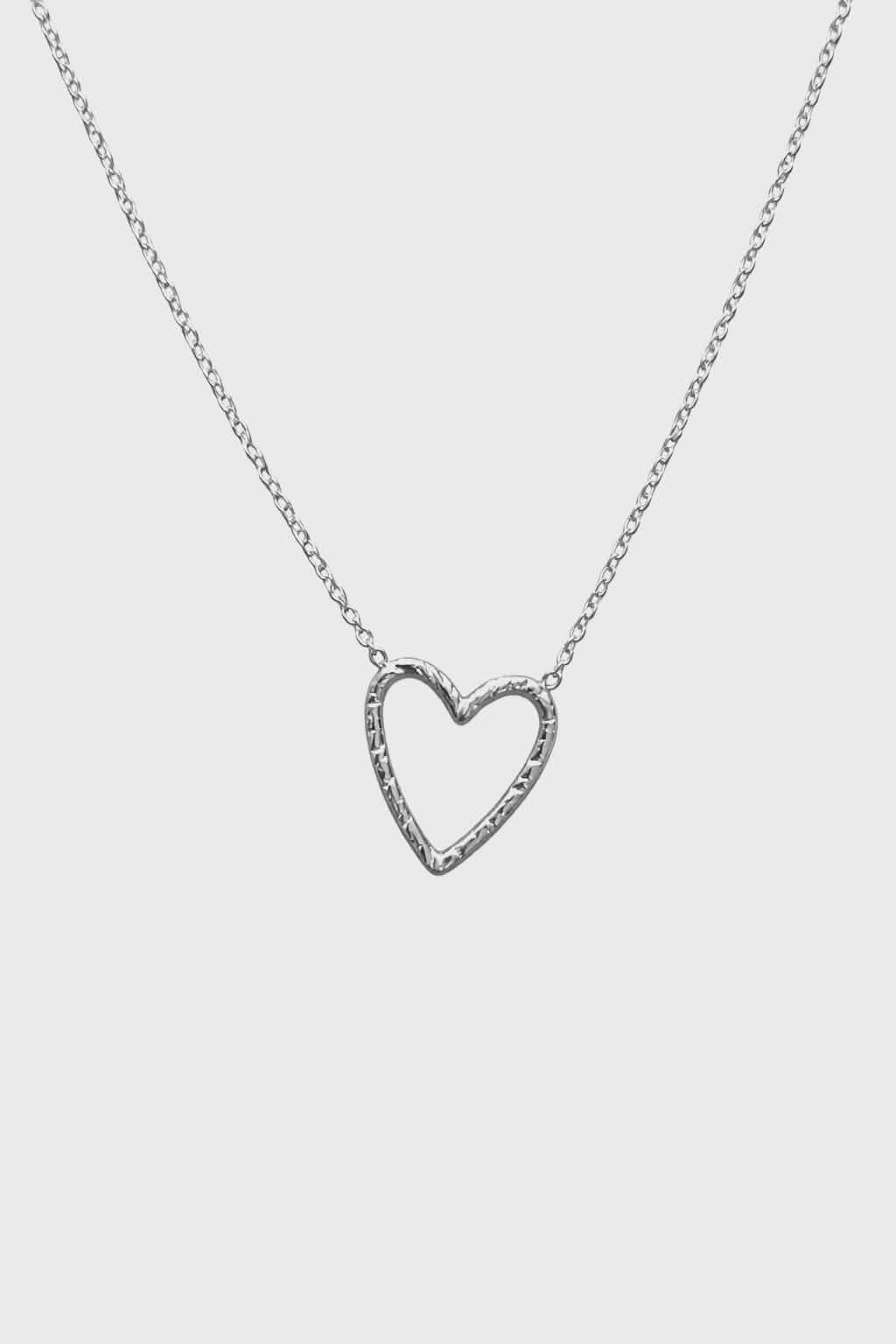 Collier cœur ajouré en acier inoxydable argenté sur fond blanc, pendentif centré au design minimaliste